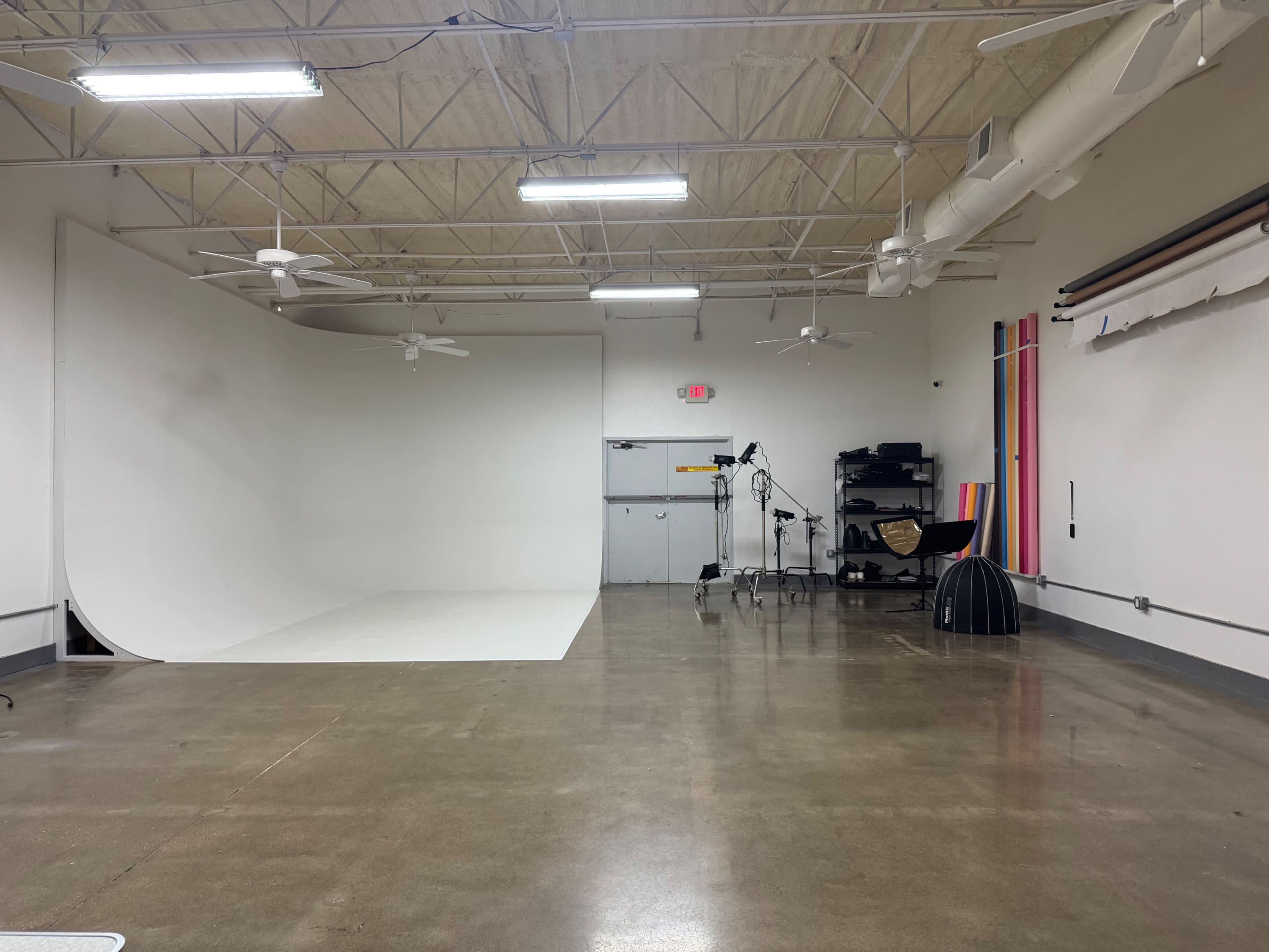 The image shows a spacious studio with a white cyclorama backdrop, photography equipment, and clean concrete floors under bright overhead lighting.
