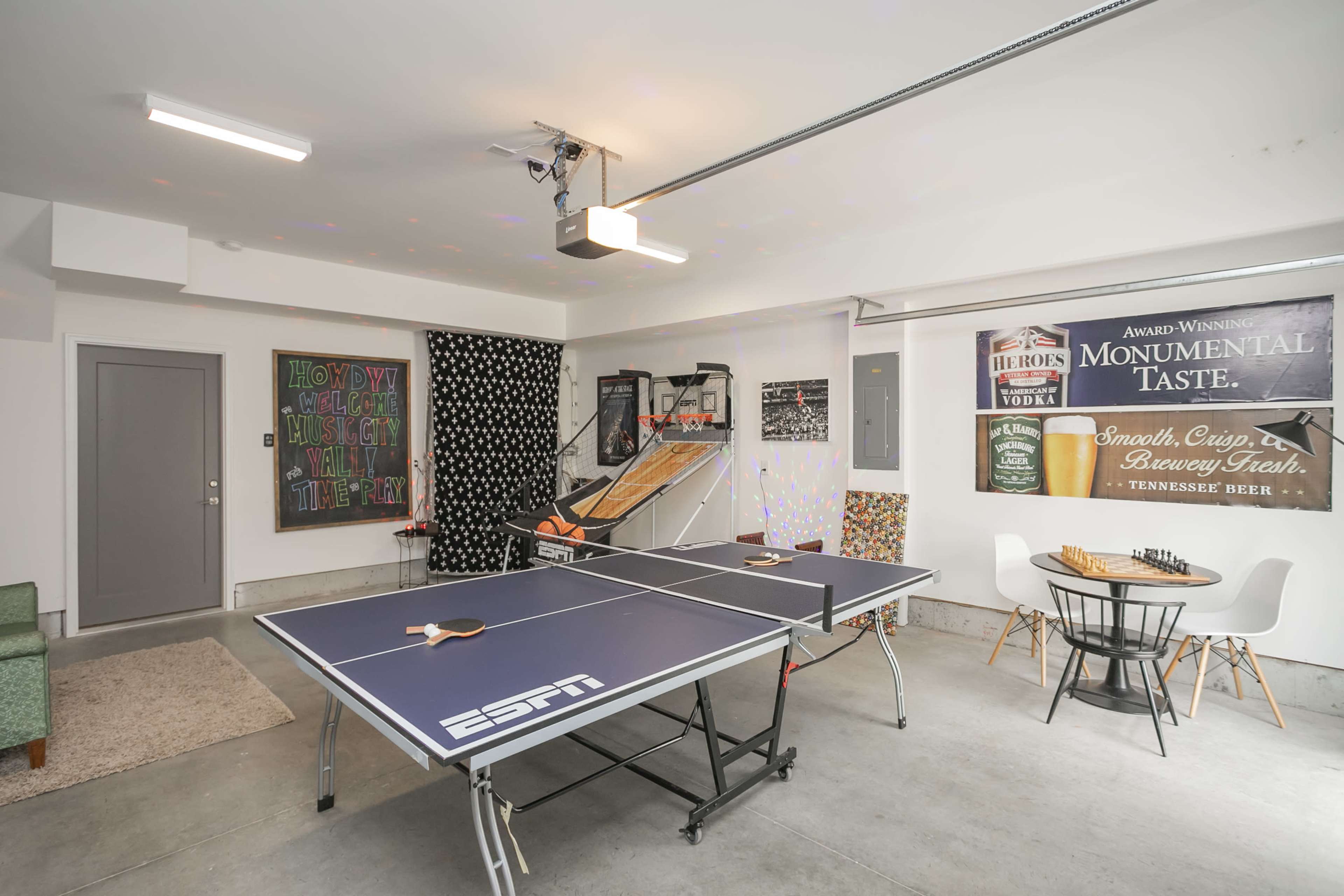 A garage converted into a recreational space featuring a ping pong table, a basketball arcade game, and various decorations on the walls.
