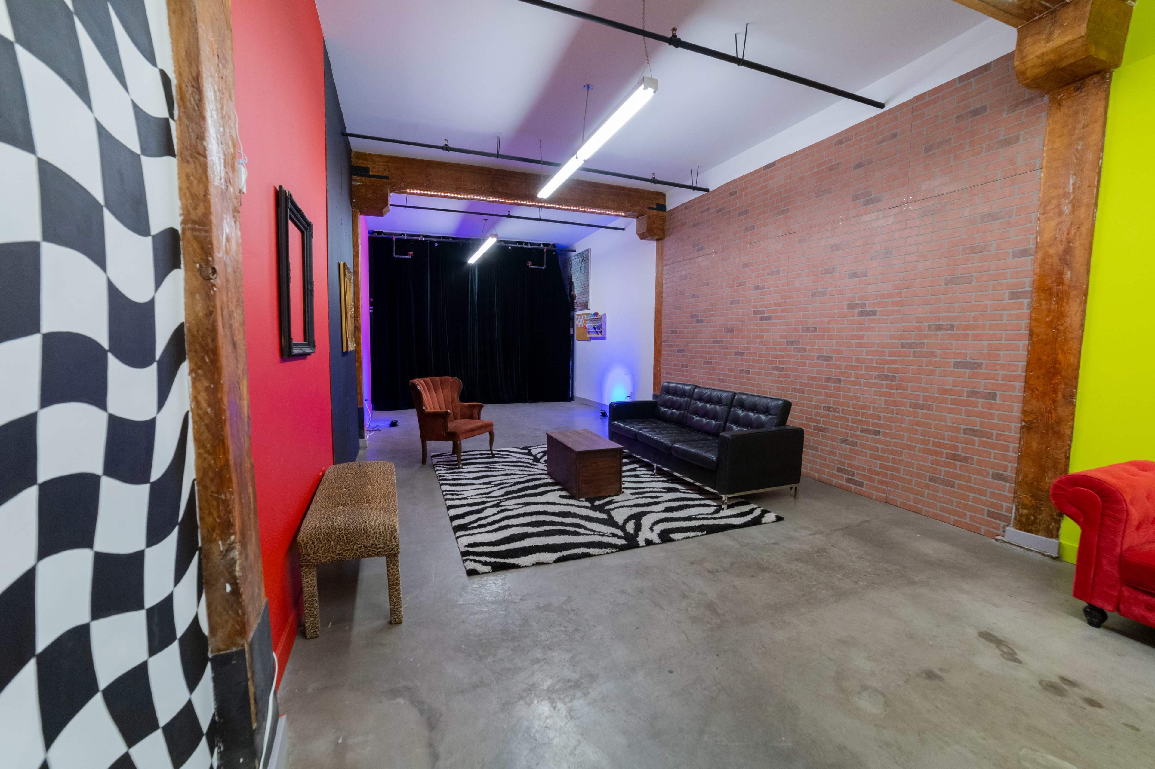 The scene shows a spacious room with exposed brick walls, a leather sofa, a wooden coffee table on a zebra-striped rug, and colorful accent walls.