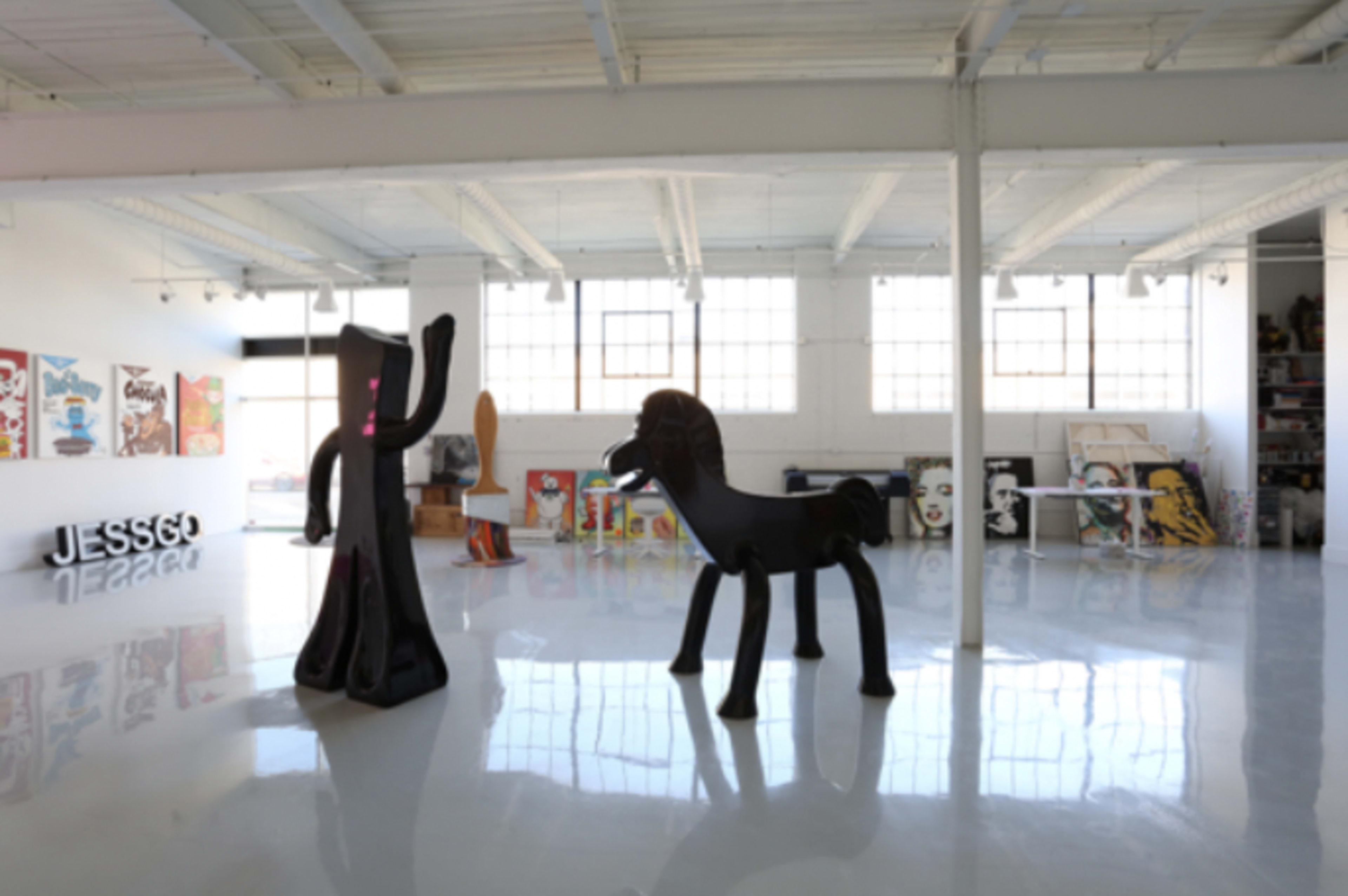 A spacious art gallery featuring large sculptures, including a black figure and a horse, with various artworks displayed on the walls.