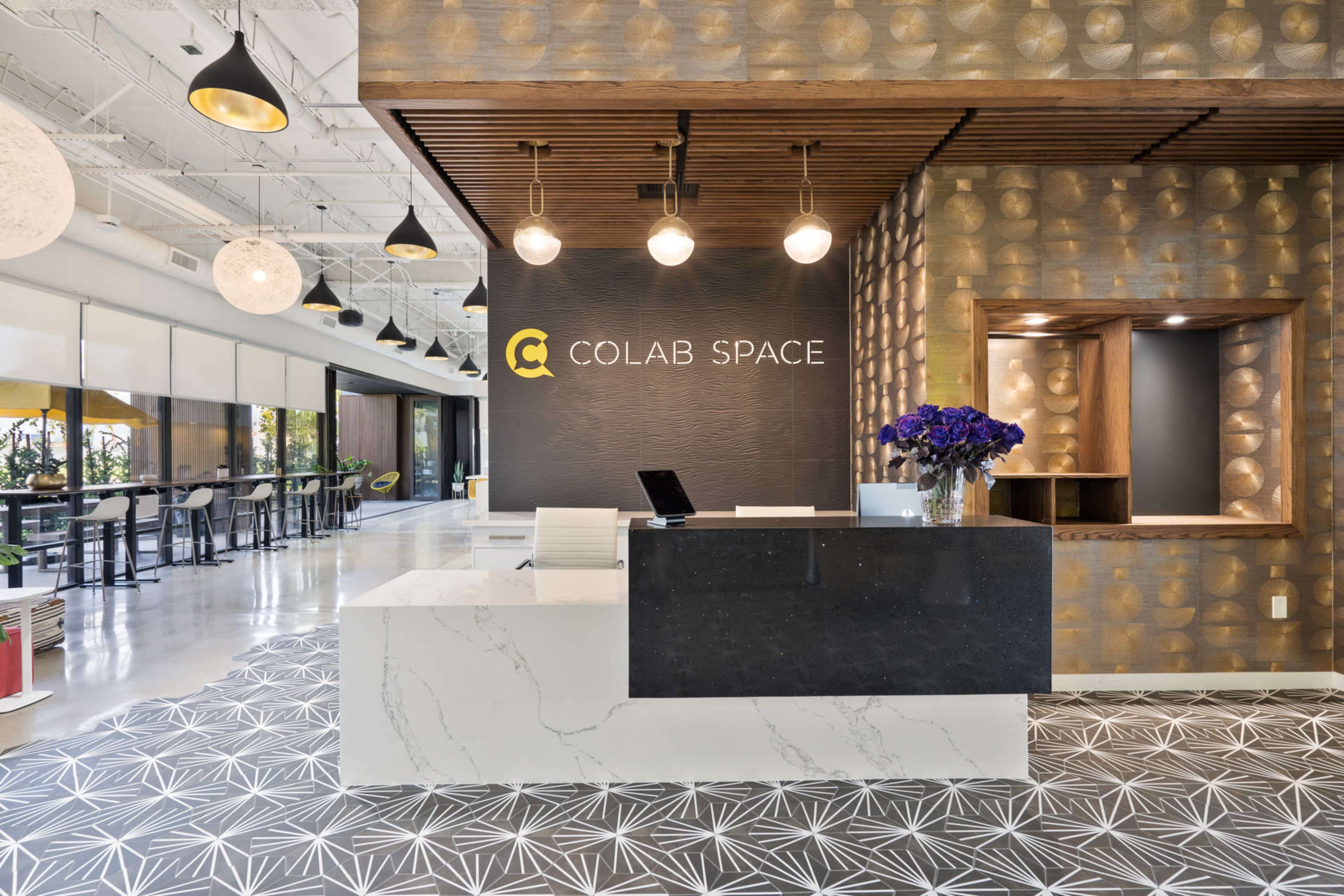 The image shows a modern office reception area featuring a sleek white marble front desk, decorative gold wall panels, and a seating area with bar stools by large windows.