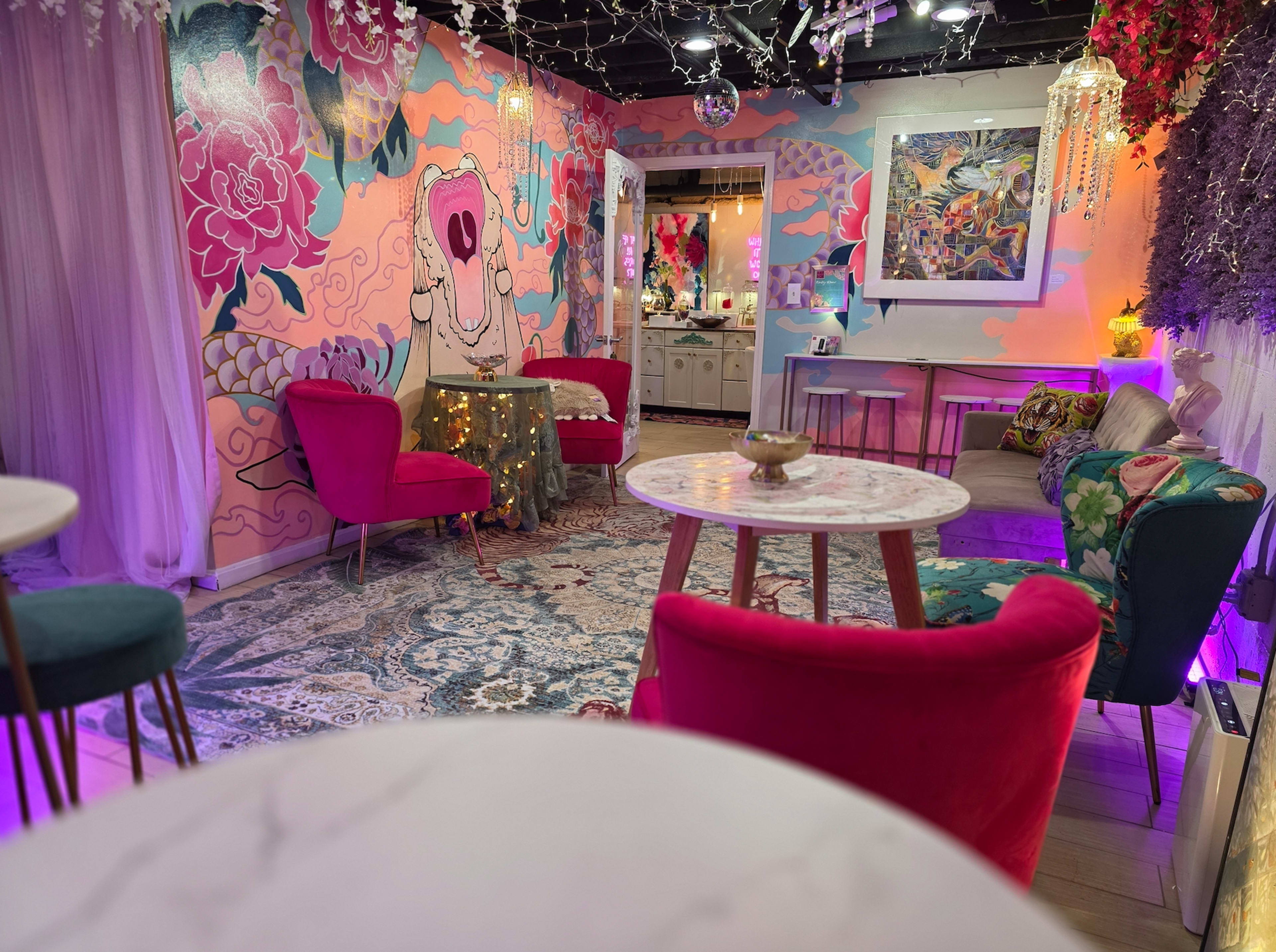 The image shows a colorful and artistic lounge area with vibrant wall murals, plush seating, and soft lighting.