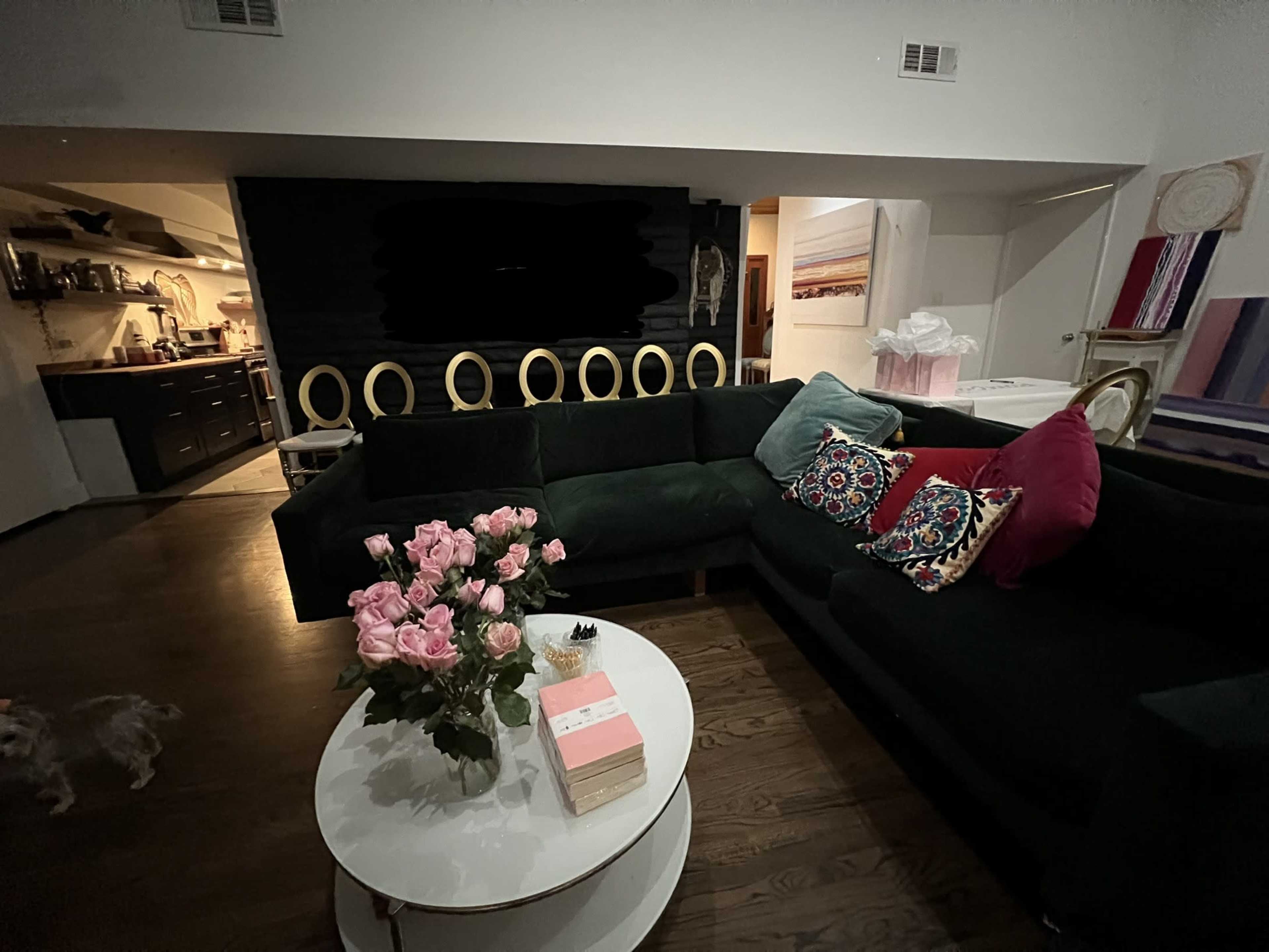 A green sectional couch with decorative pillows surrounds a round coffee table adorned with a bouquet of pink roses.