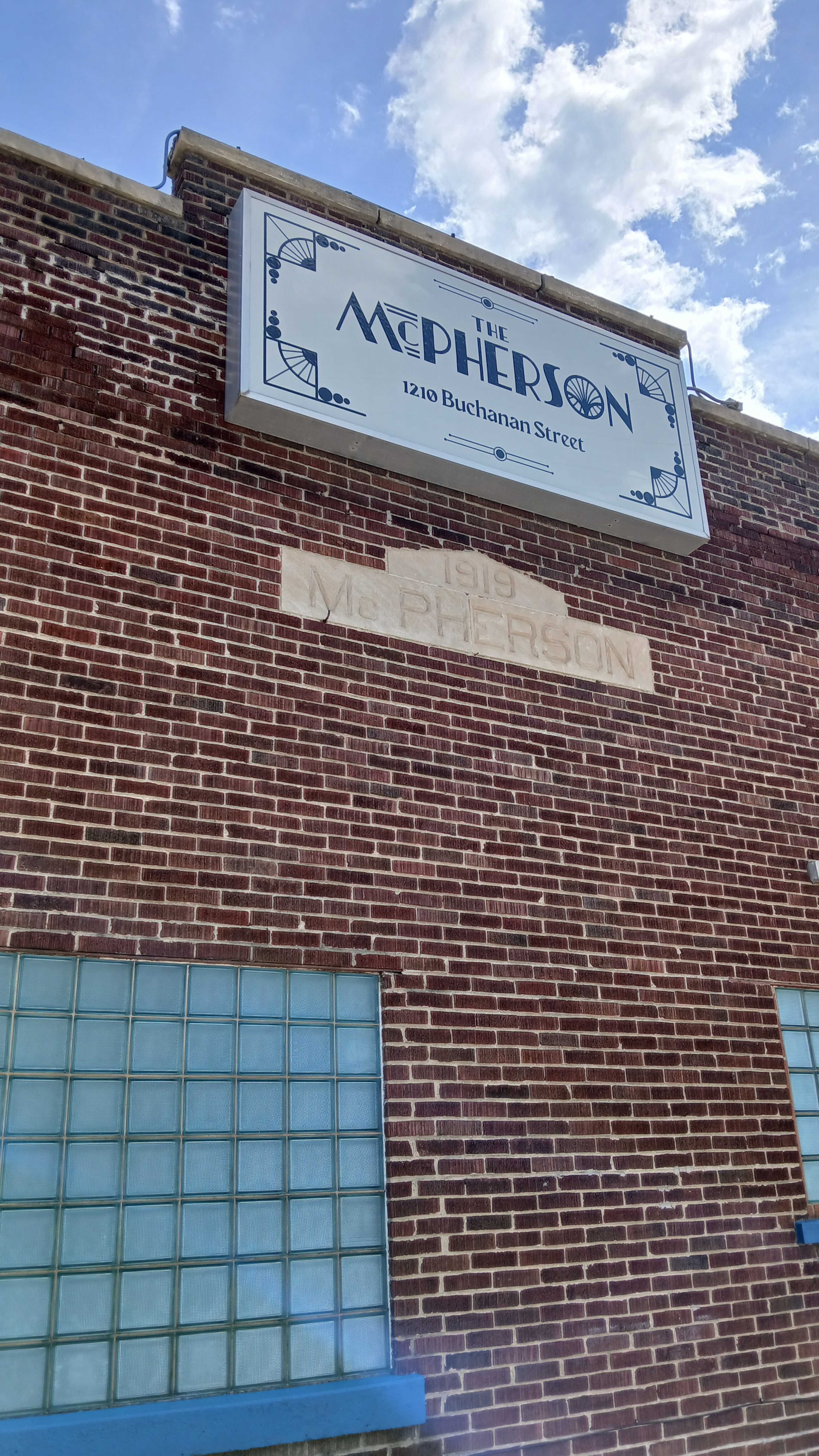 The image shows a brick building with a sign that reads "THE McPHERSON" above the entrance, and the year "1913" engraved in the brick below.