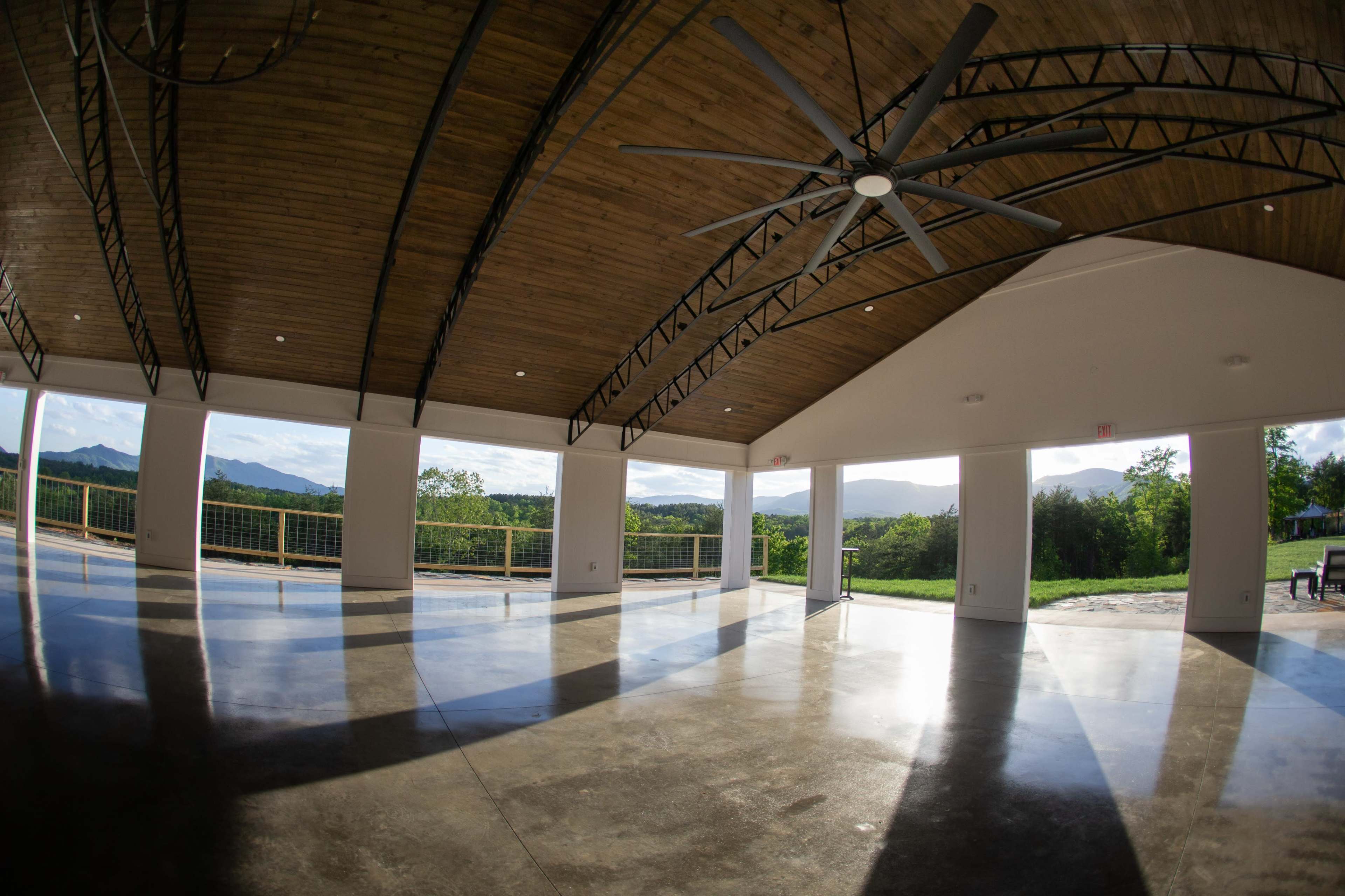 A spacious, empty room with large windows and a high vaulted ceiling, offering a view of mountains in the distance.