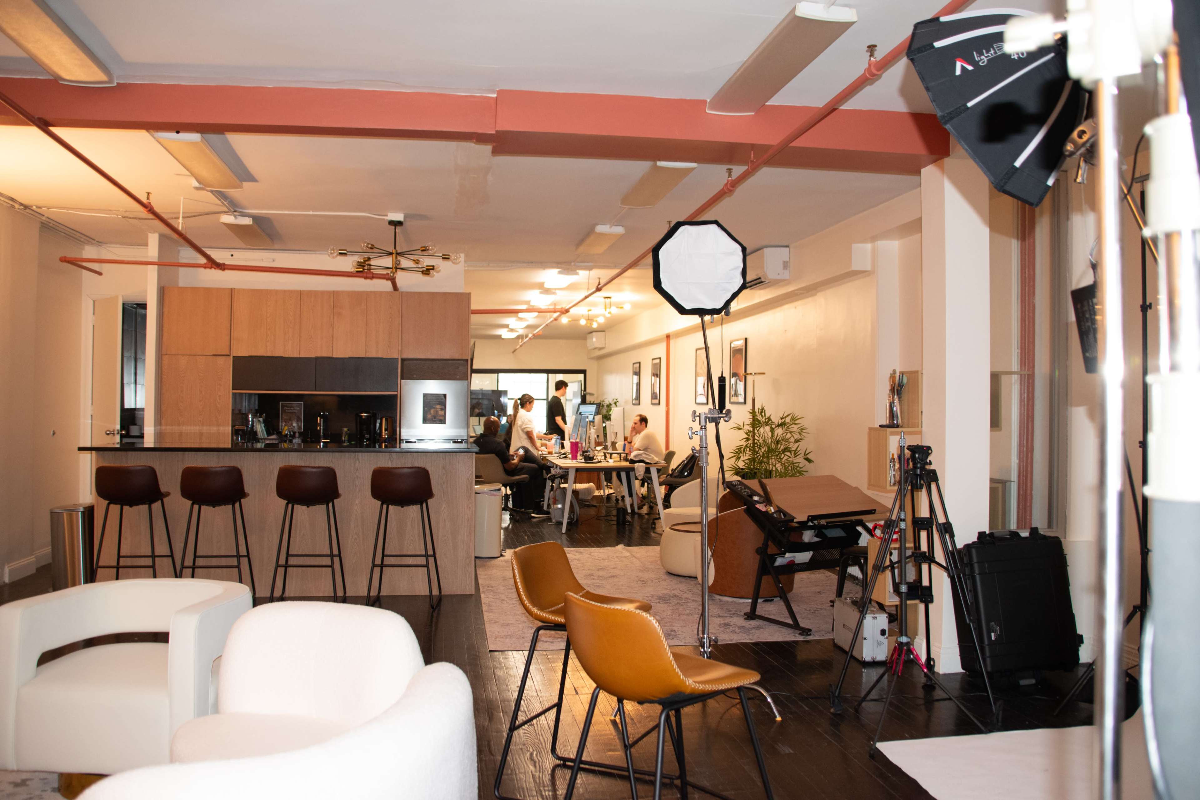 A modern kitchen and living area are visible, with bar stools at a counter, a dining table, and various photography equipment set up in the foreground.
