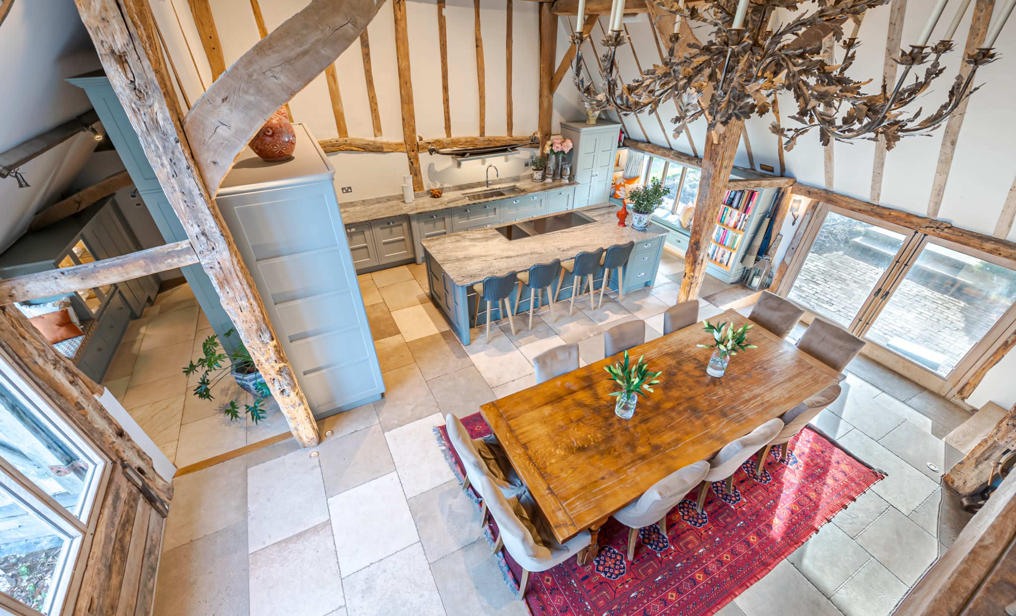 A spacious kitchen and dining area featuring a large wooden table surrounded by upholstered chairs, a gray kitchen island, and exposed timber beams.