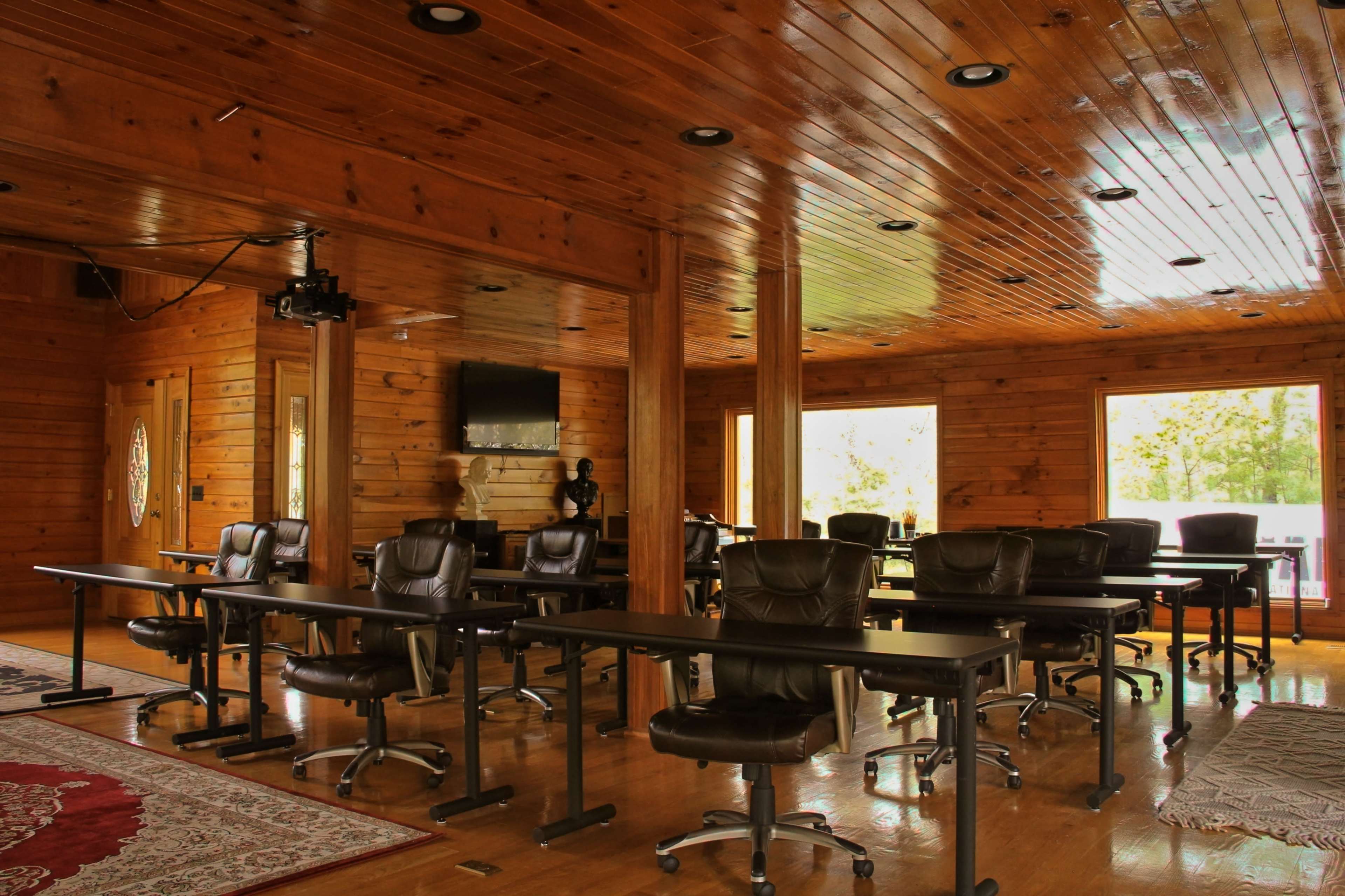 A spacious wooden room set up with several black office chairs and tables, featuring large windows that let in natural light.