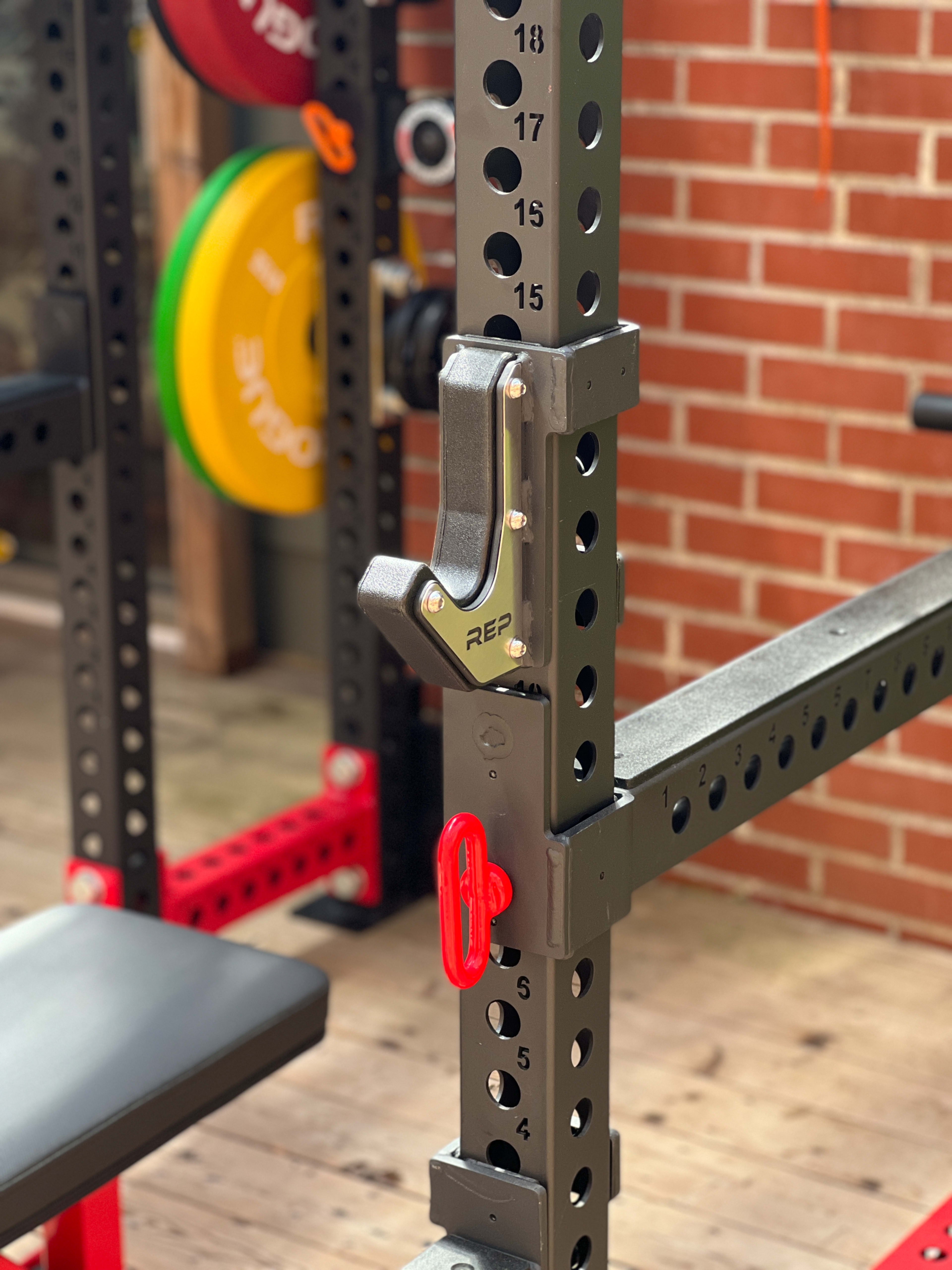 A close-up of a weightlifting rack with adjustable safety bars and color-coded weight plates in the background.