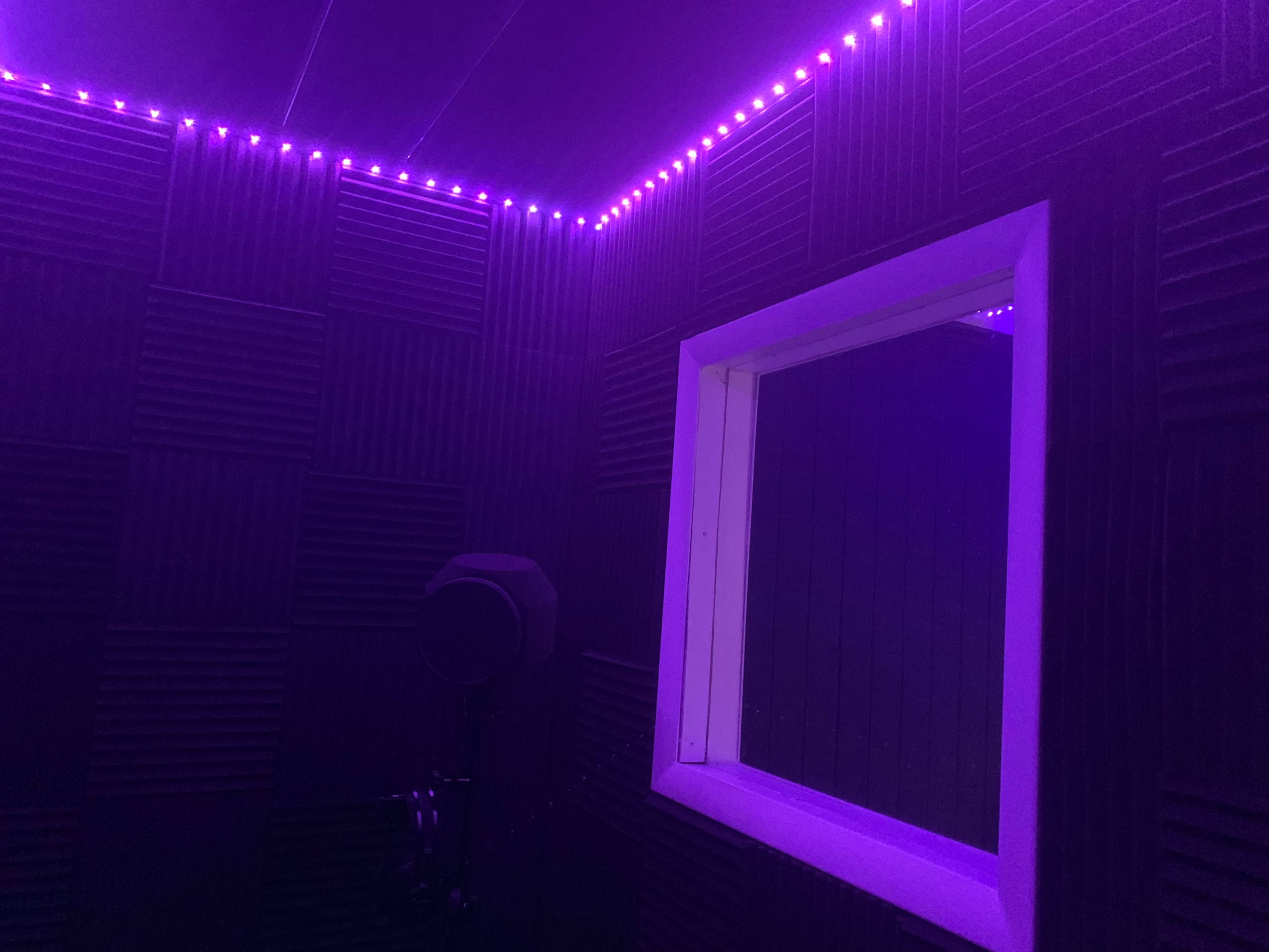 A soundproof recording booth with purple LED lighting and a window view.