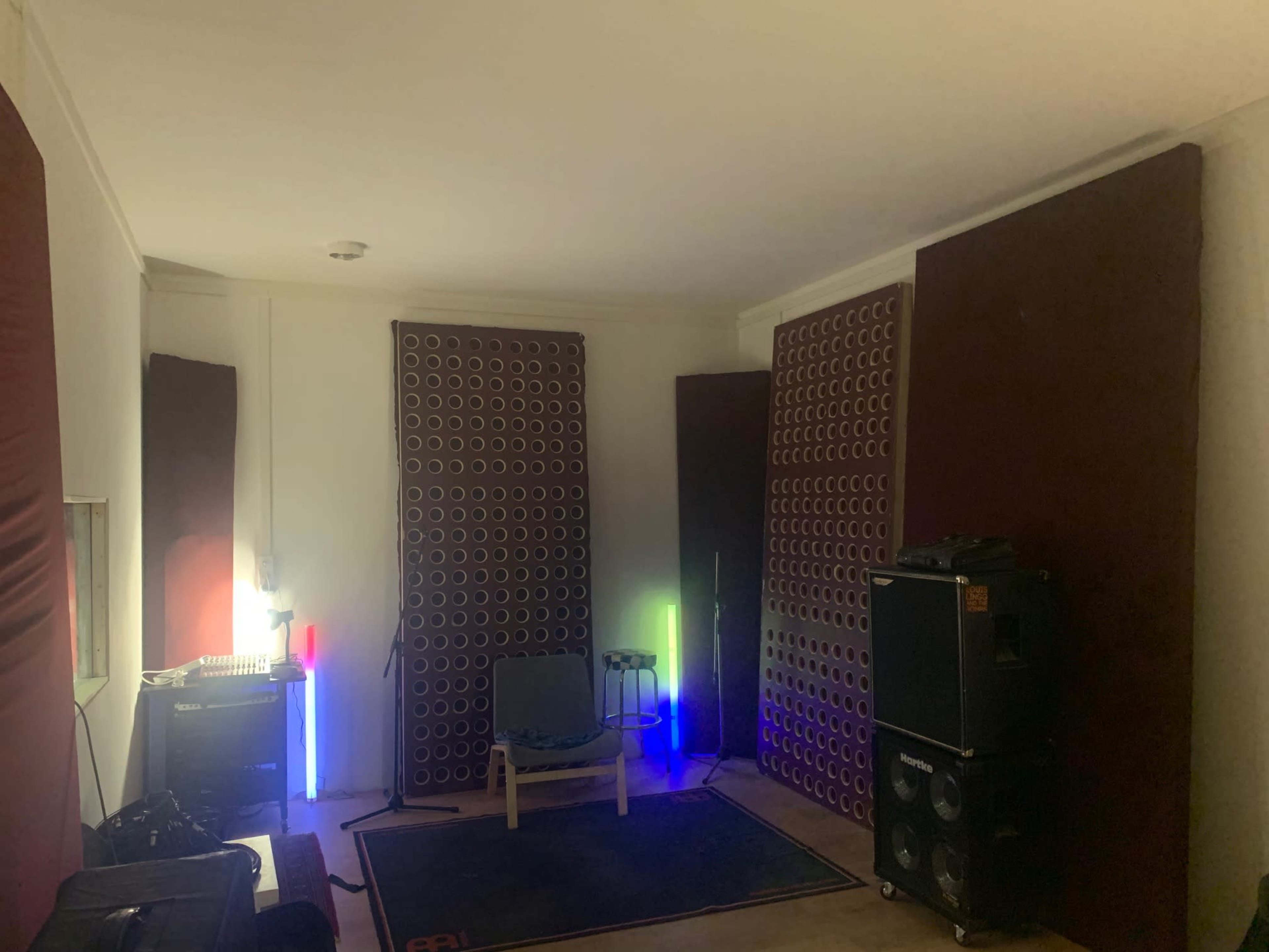 A soundproofed music studio with acoustic panels, a chair, and audio equipment illuminated by colorful lights.