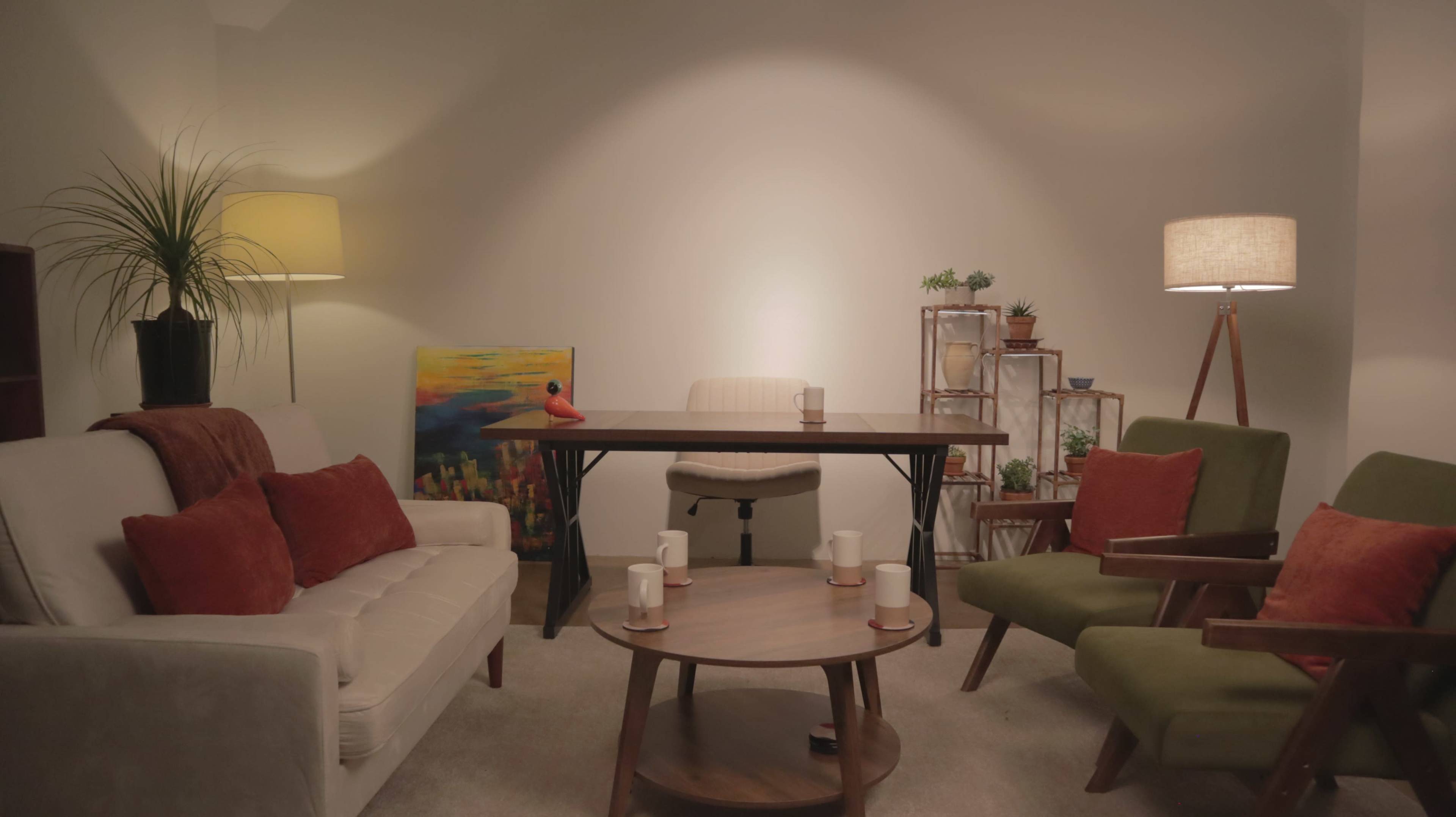 The image shows a cozy room with a table surrounded by chairs, a sofa, and various plants, illuminated by lamps.