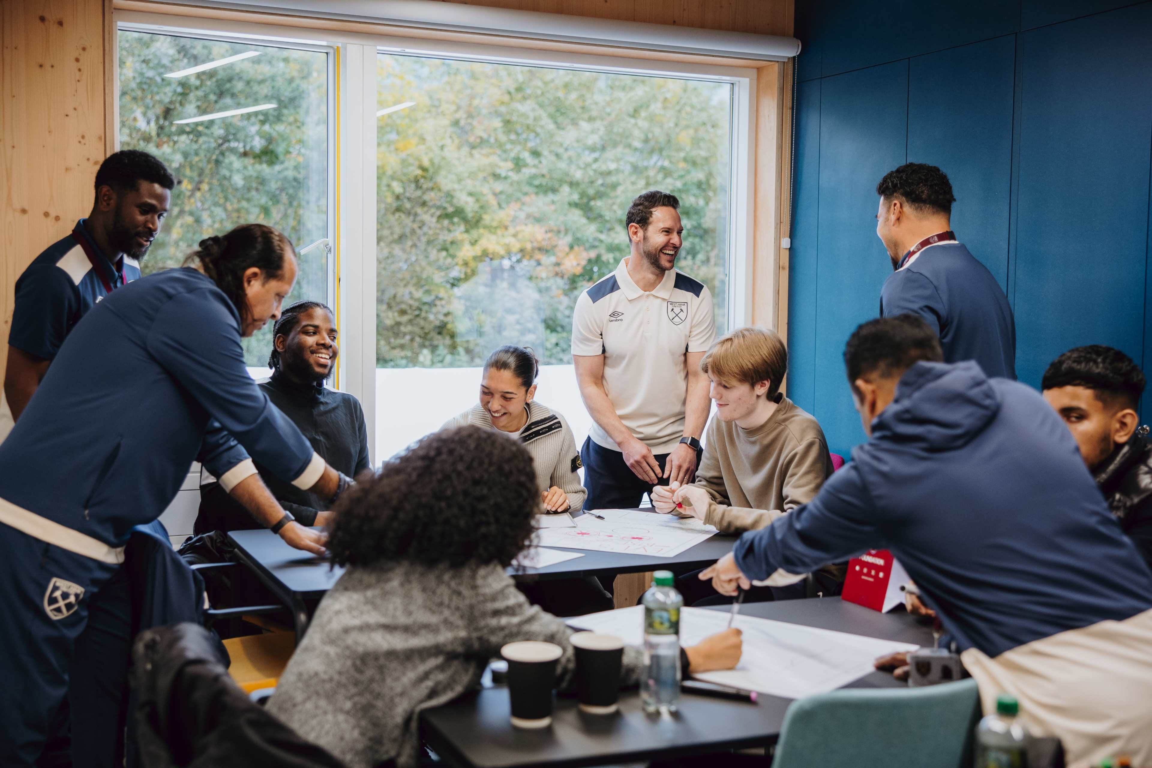 A group of people is gathered around tables in a room, engaging in a collaborative discussion and working on paper materials.