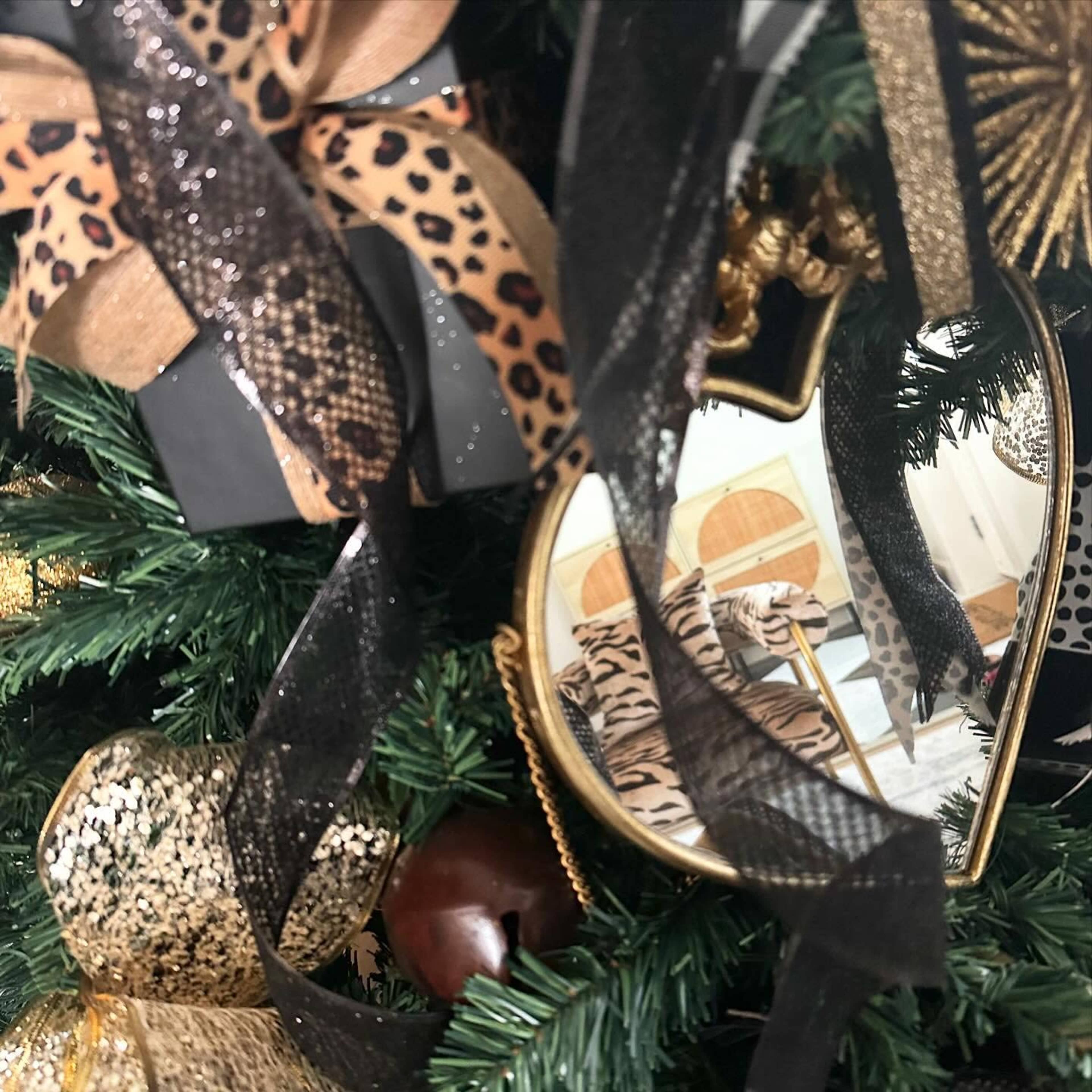 A decorated Christmas tree featuring leopard-print bows, gold accents, and a heart-shaped mirror among the ornaments.