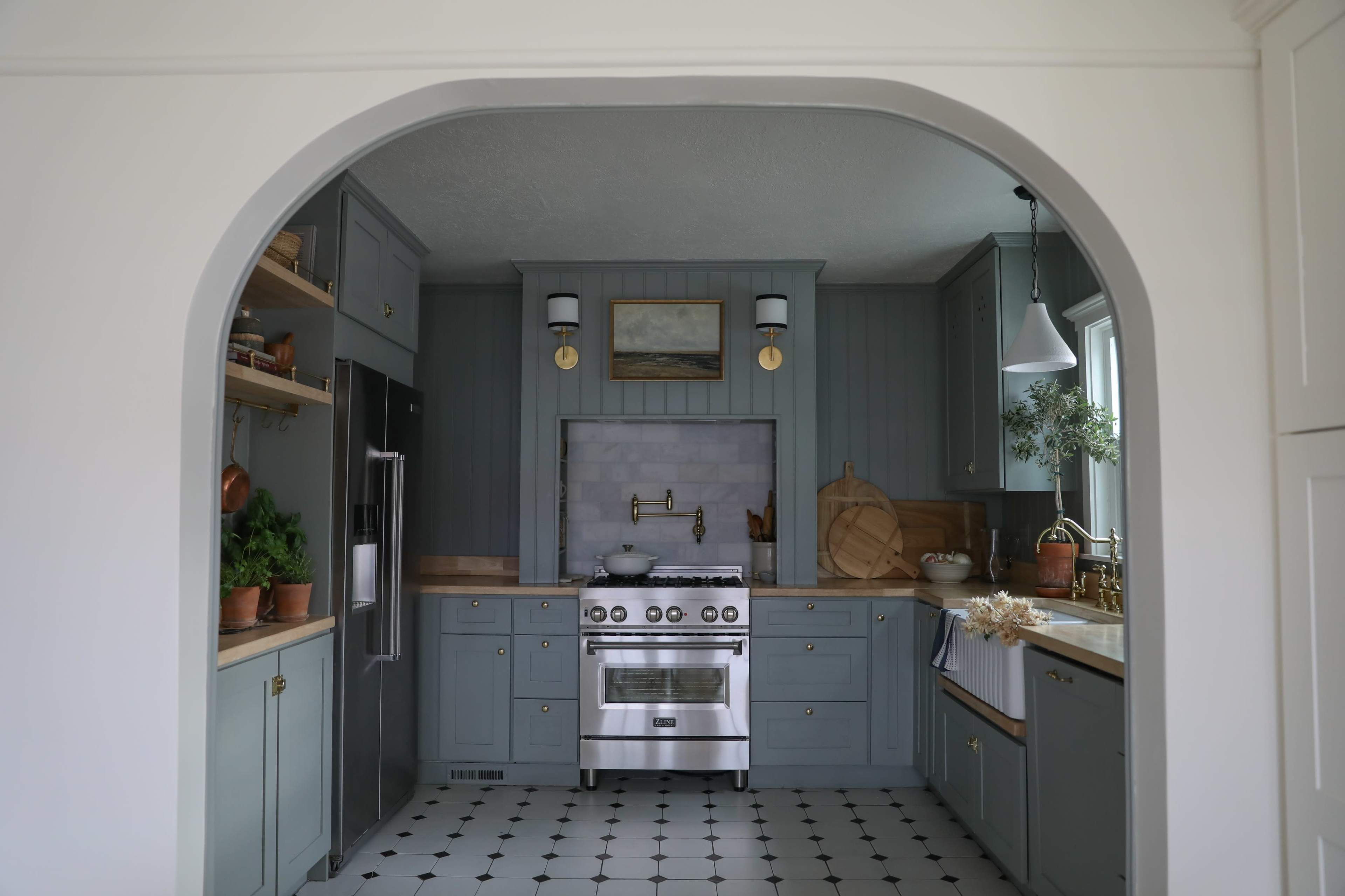 The image shows a modern kitchen with gray cabinetry, stainless steel appliances, and white tile flooring featuring black accents.