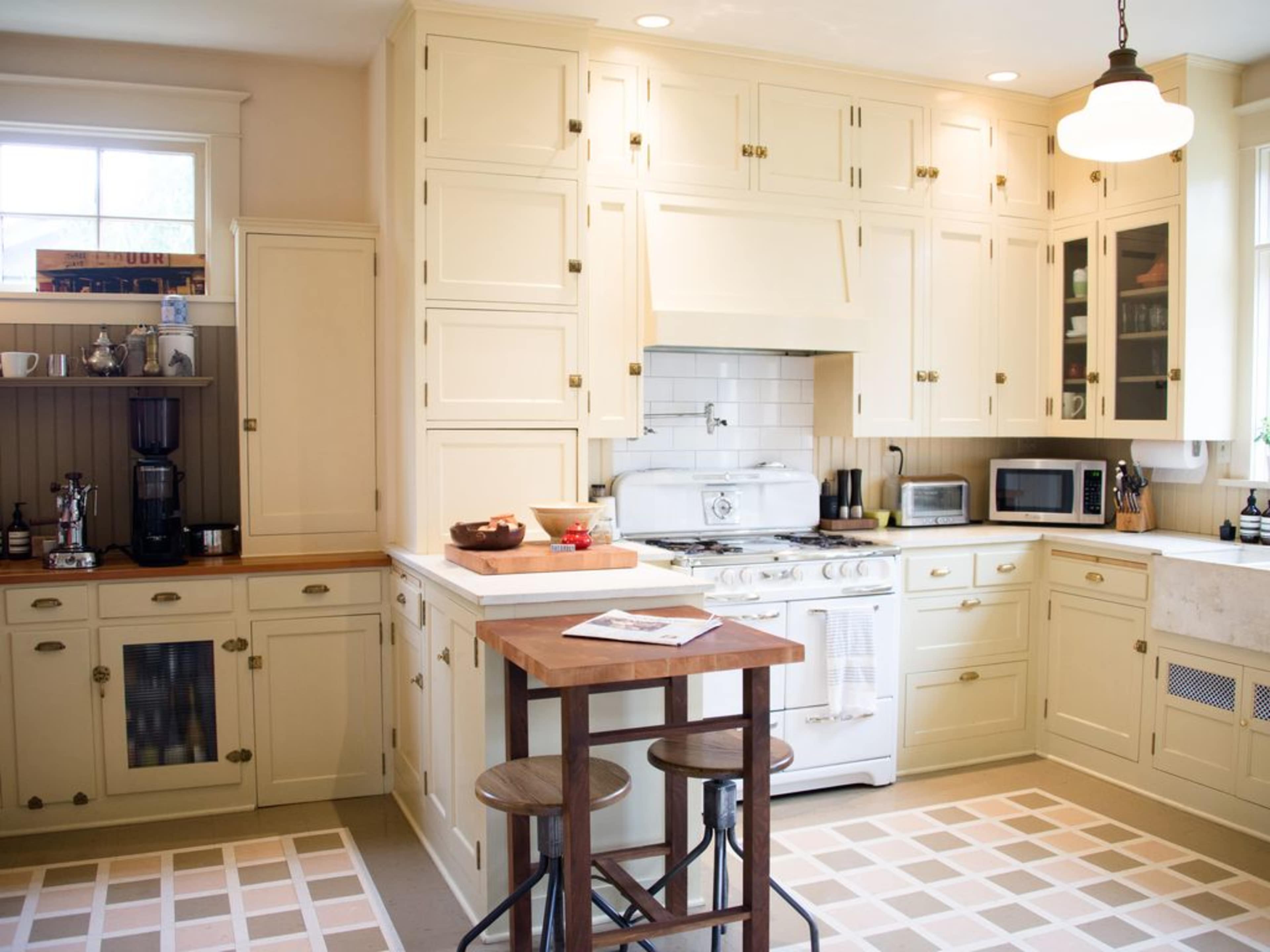 A well-lit kitchen with cream-colored cabinets, a white stove, and a wooden table with two stools.