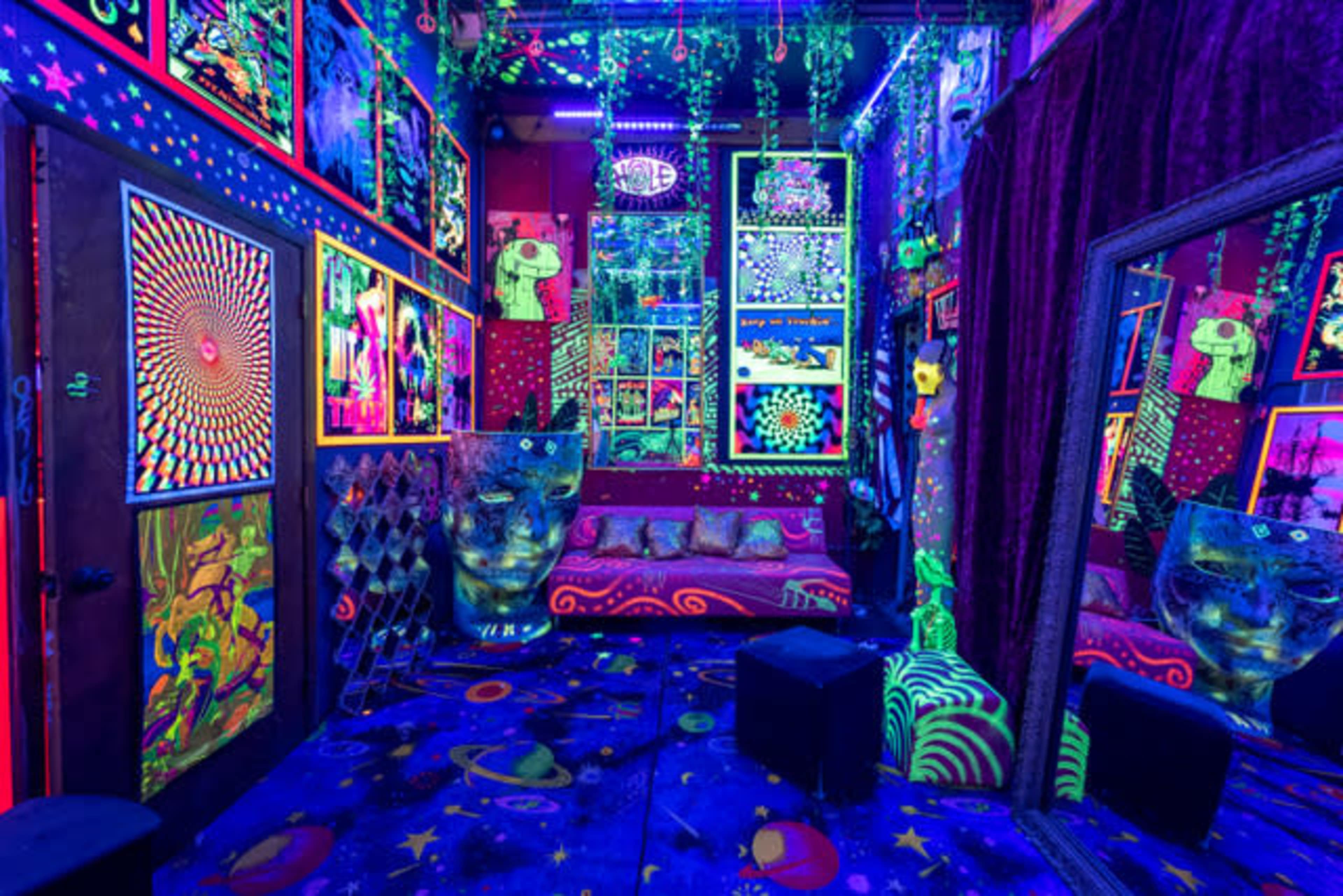 A vibrant room decorated with fluorescent art, hanging plants, and a starry patterned floor under blacklight.