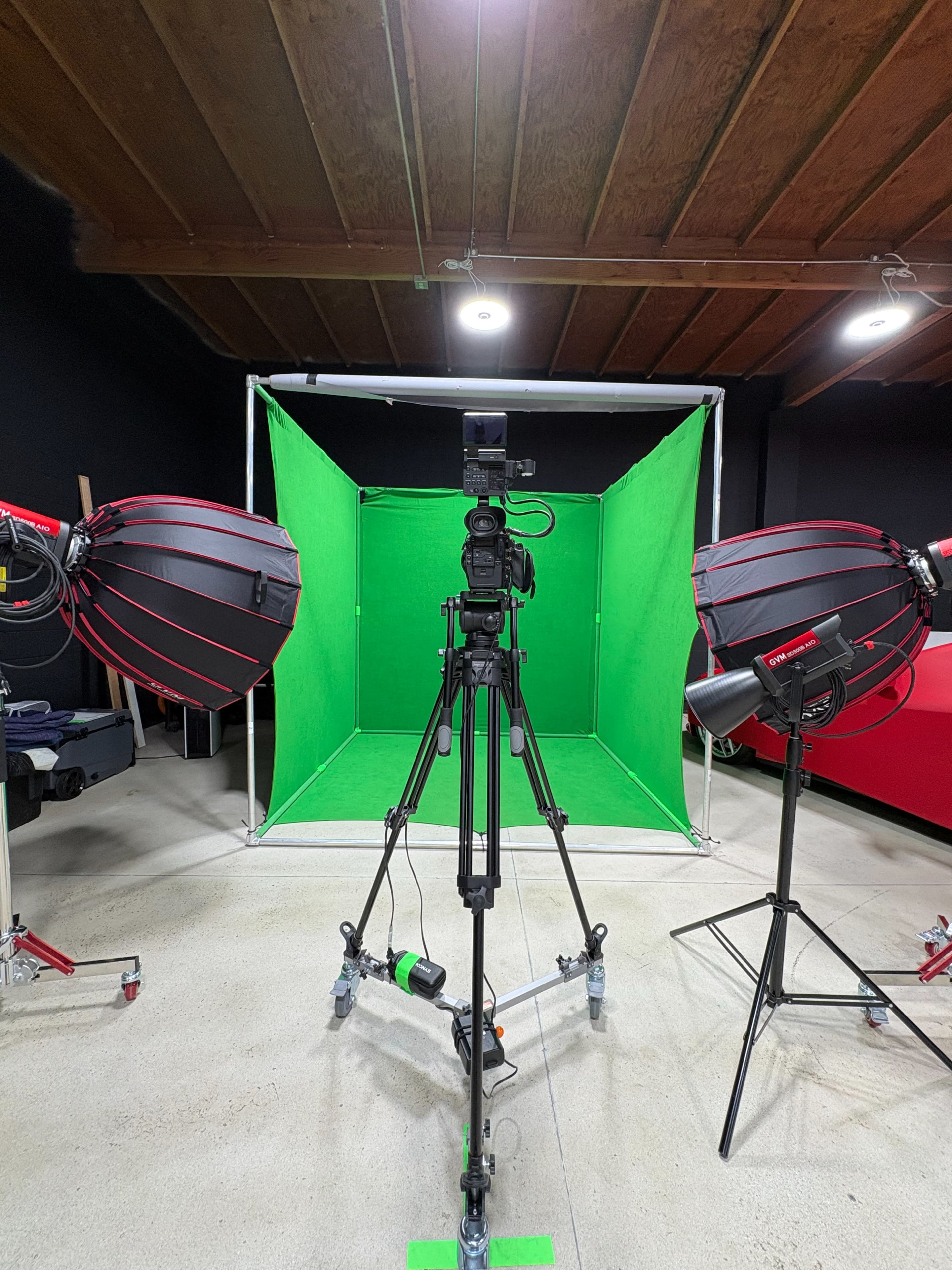 The image shows a studio setup with a camera on a tripod facing a green screen, flanked by two softbox lights.