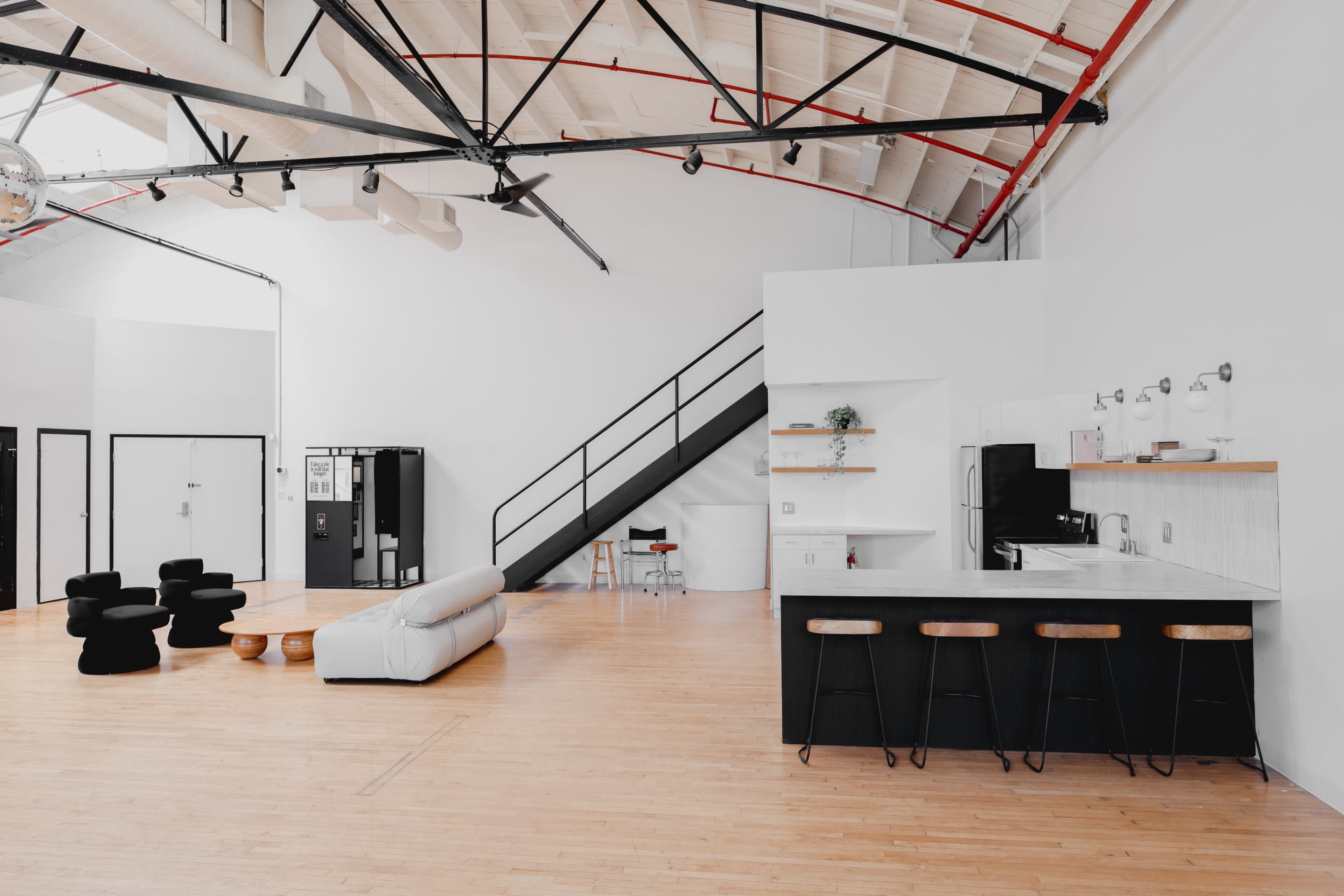 A spacious, modern open-plan living area with a kitchen, seating area, and a staircase leading to an upper level.