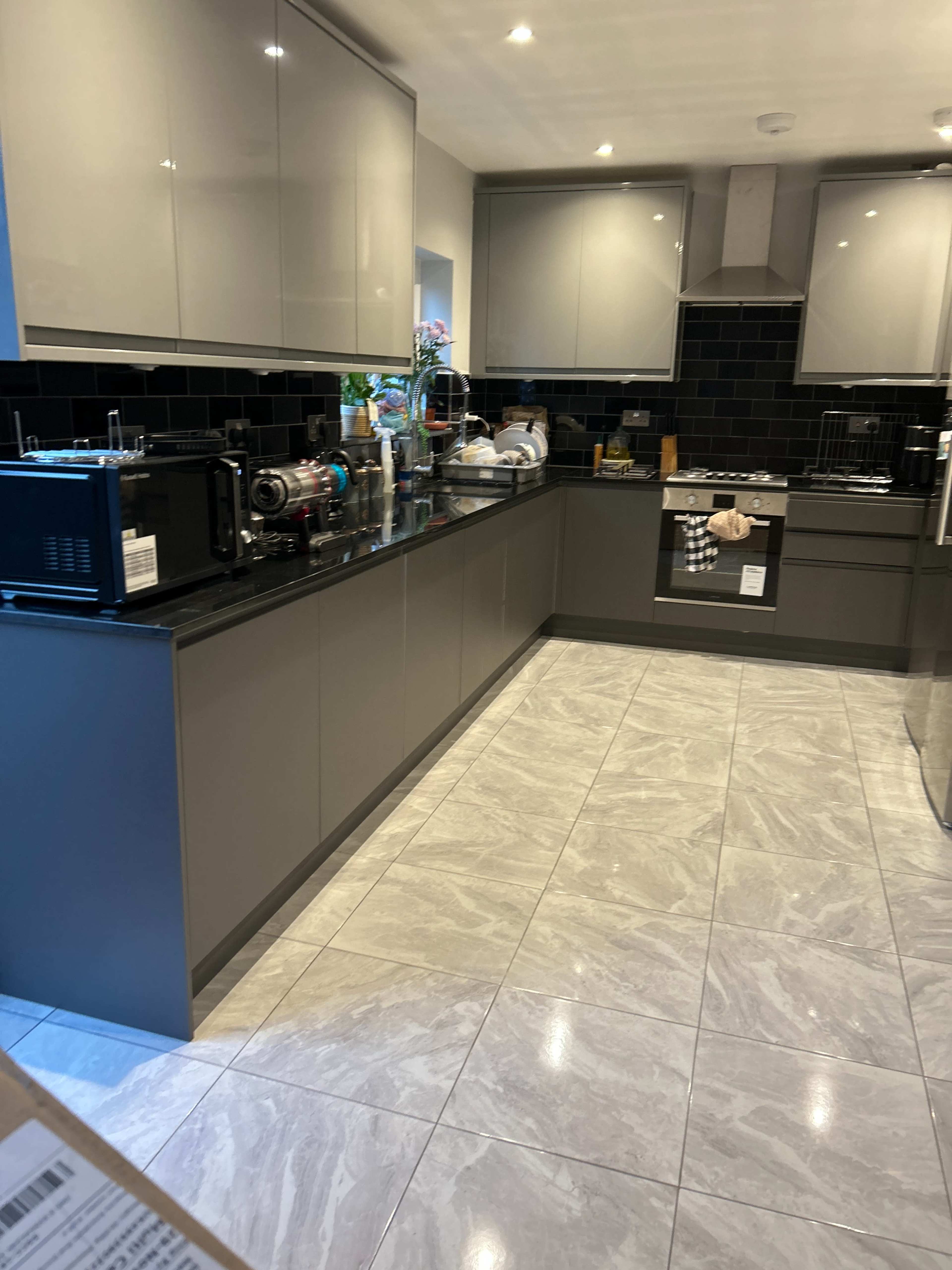 A modern kitchen with gray cabinets, a black tile backsplash, and a shiny tiled floor.