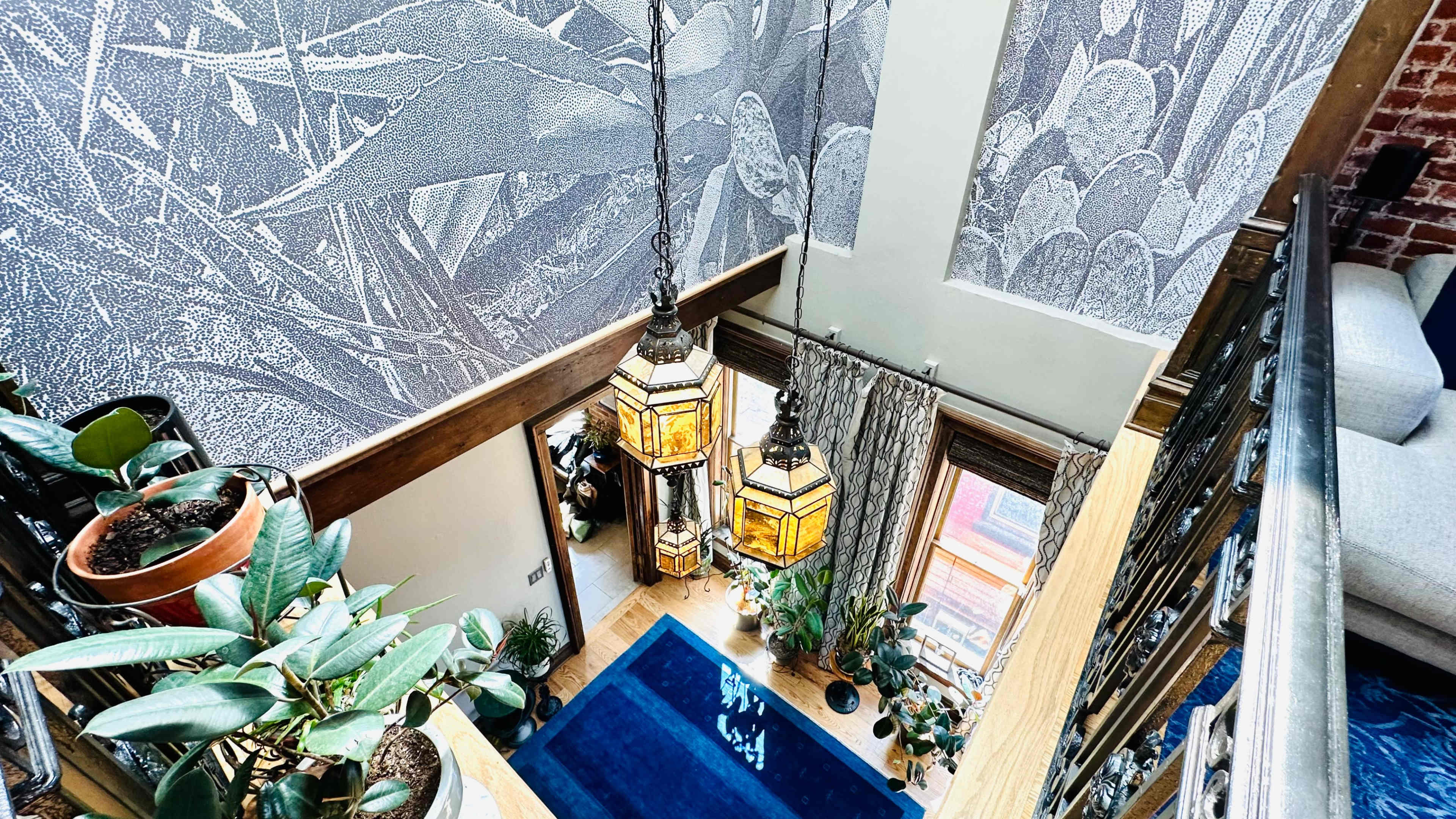 A stairwell with patterned wallpaper, two decorative lanterns hanging from the ceiling, and various plants arranged in the space.