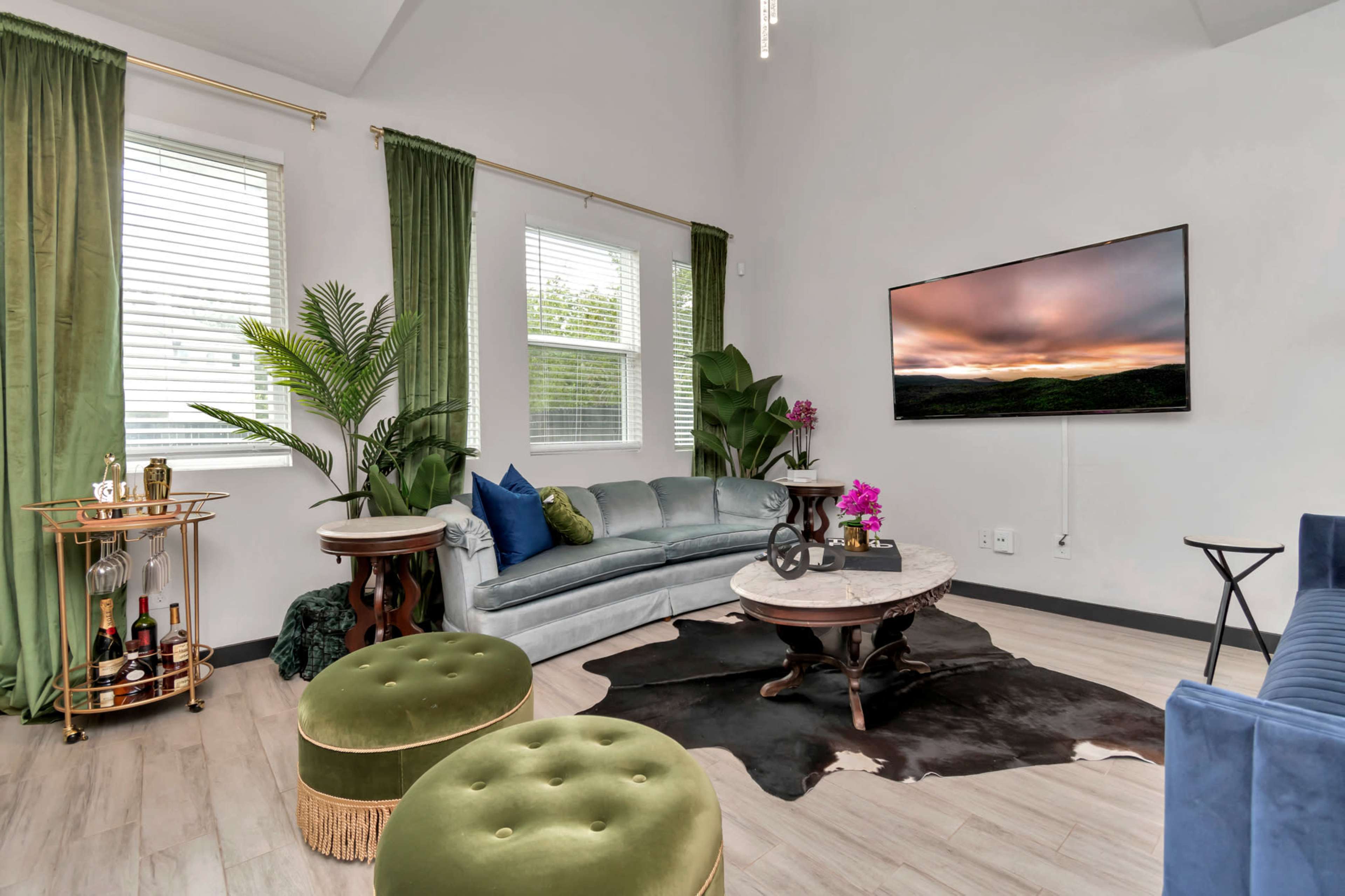A modern living room with a sectional sofa, a round coffee table, a bar cart, and green curtains.