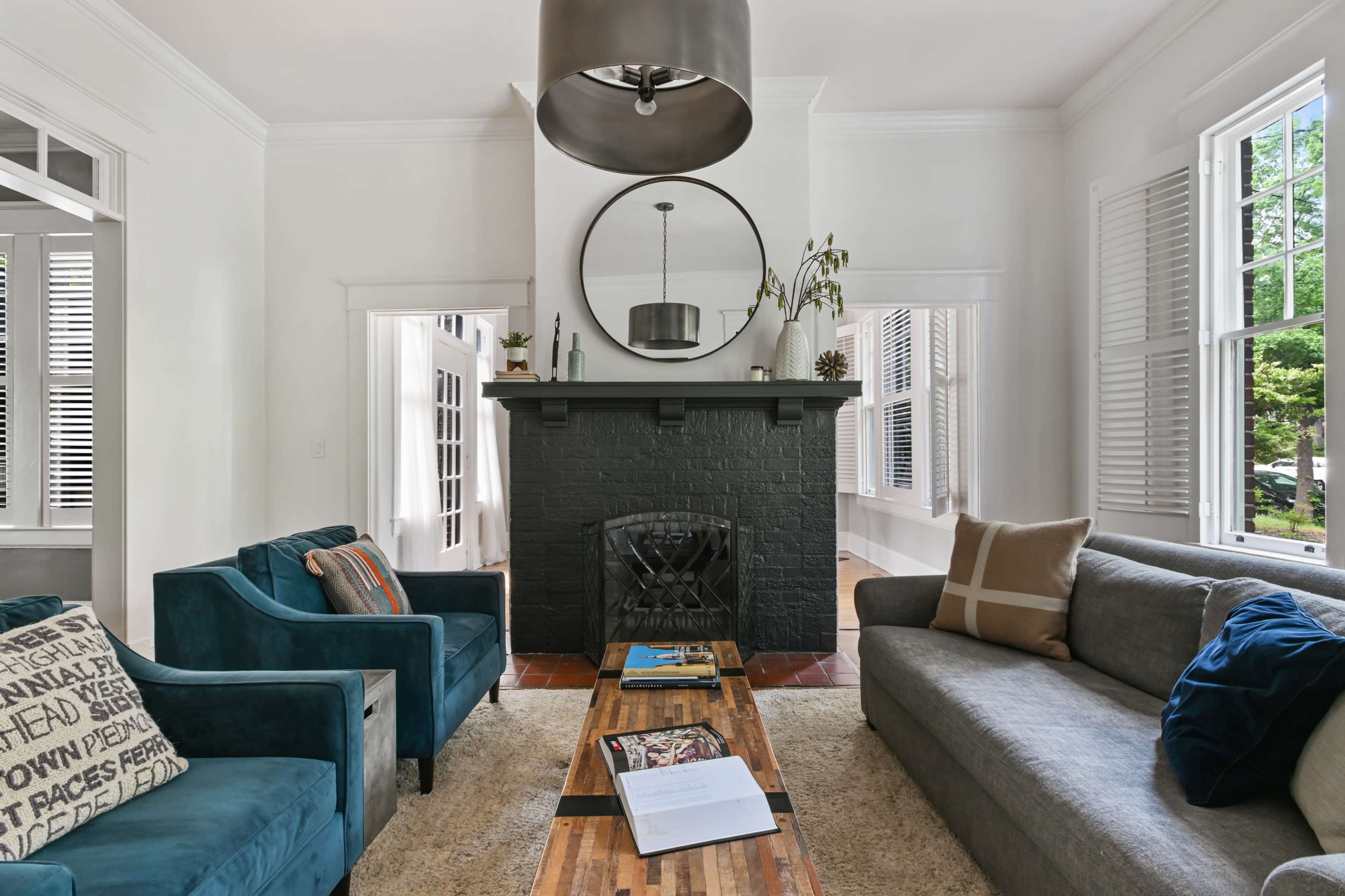 The image shows a modern living room with two sofas, a coffee table, and a black fireplace featuring a round mirror above it.