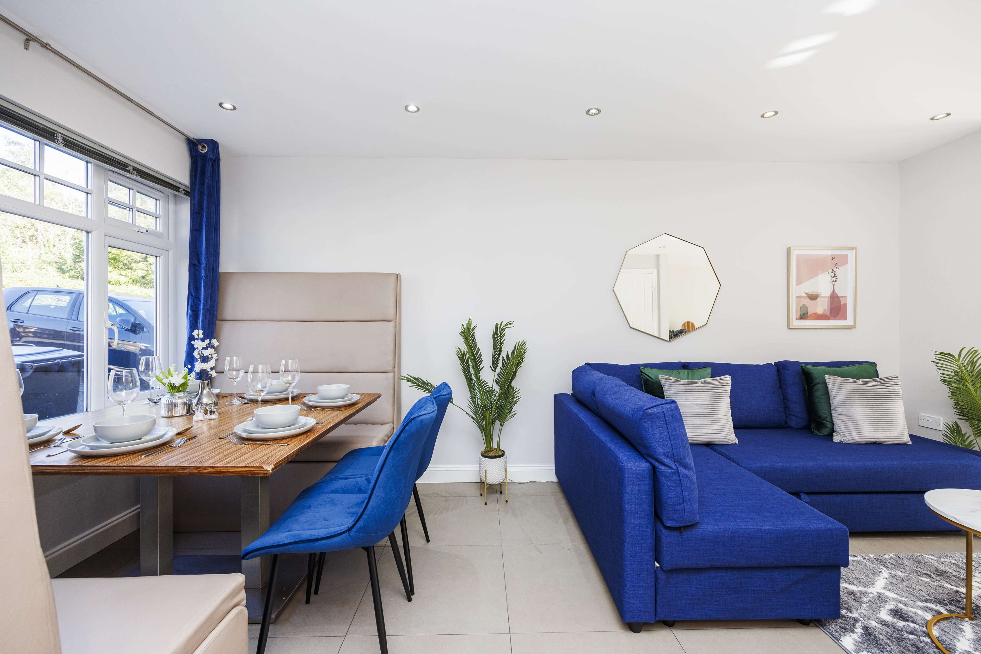 A modern dining area with a wooden table set for a meal, blue chairs, and a blue sofa against a light-colored wall.