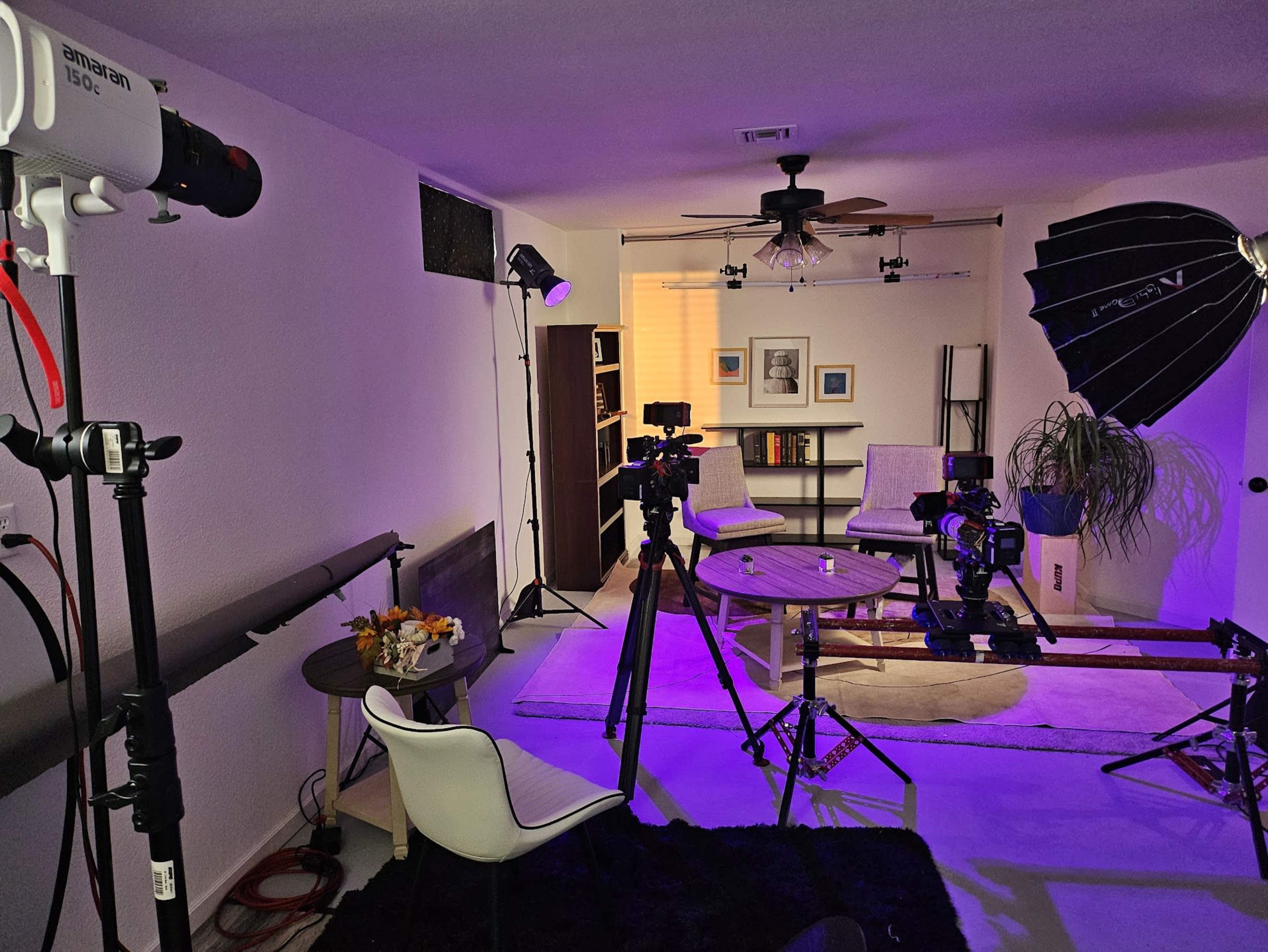 A well-equipped studio setup features various lighting fixtures, cameras, and a small table in a modern living space.