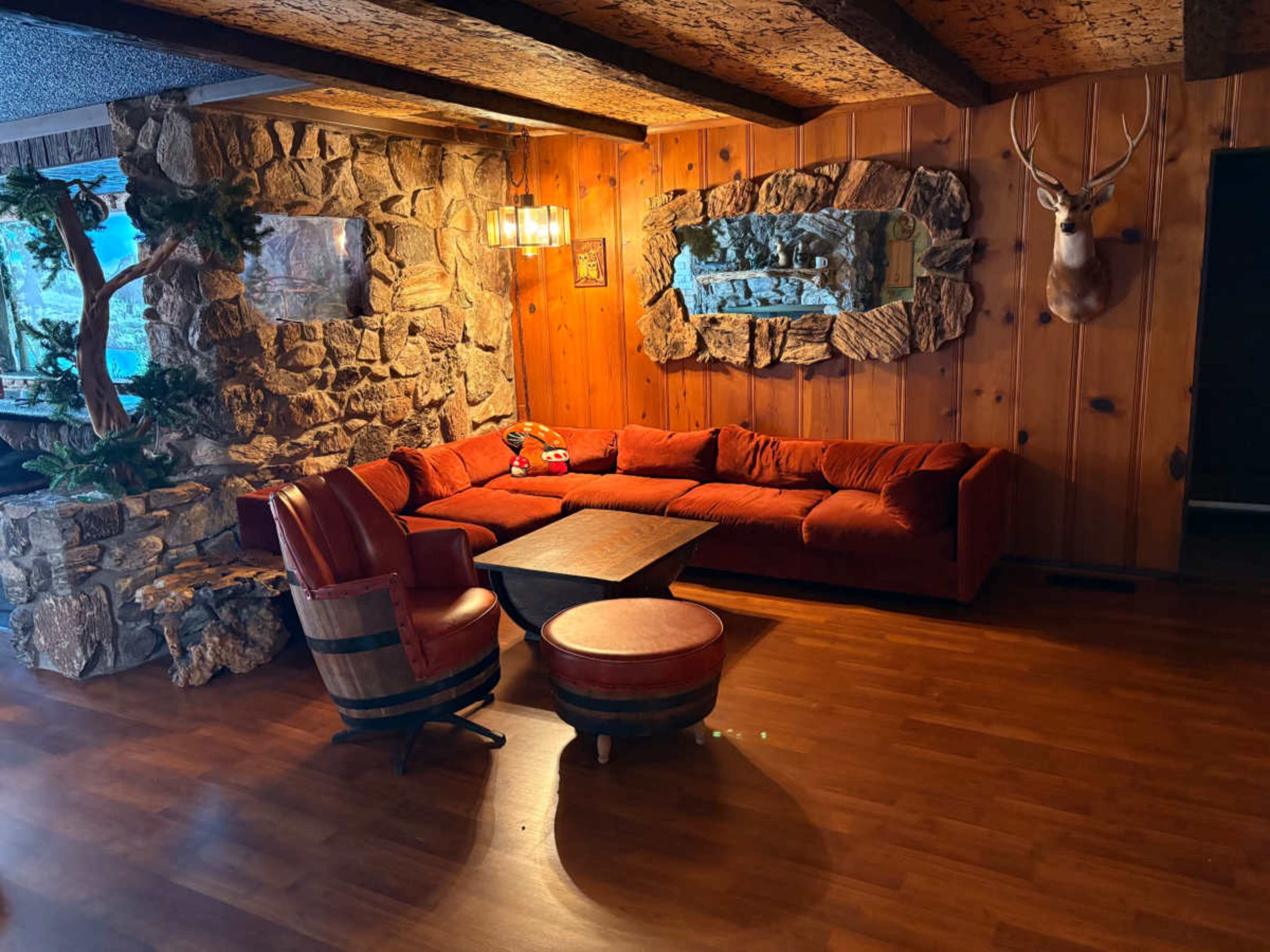 The image depicts a living room with a red sofa, wooden walls, a stone feature wall, and rustic decor items including a deer head mounted on the wall.