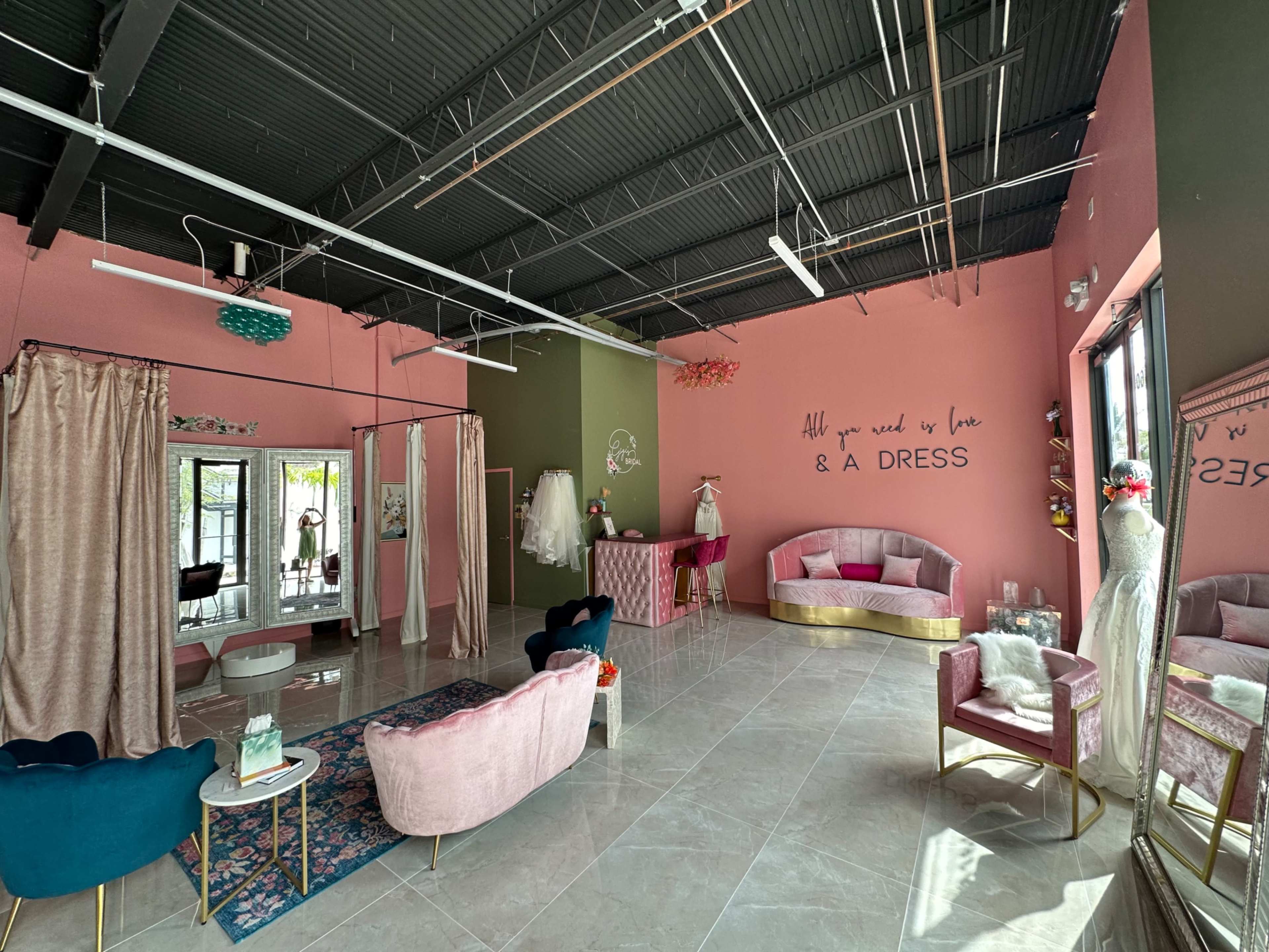 The image shows a boutique interior with pink and green walls, featuring elegant seating, a dress display, and a large window.