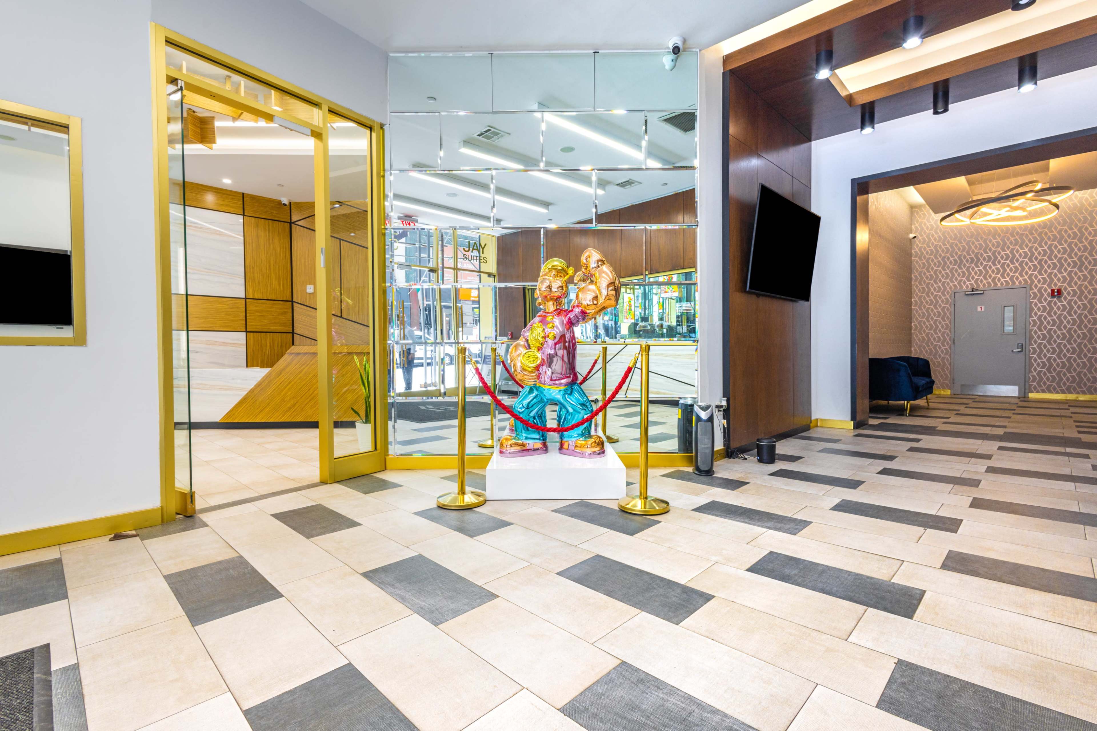 The image shows a modern lobby featuring a colorful statue, glass doors, and tiled flooring with a lounge area visible in the background.