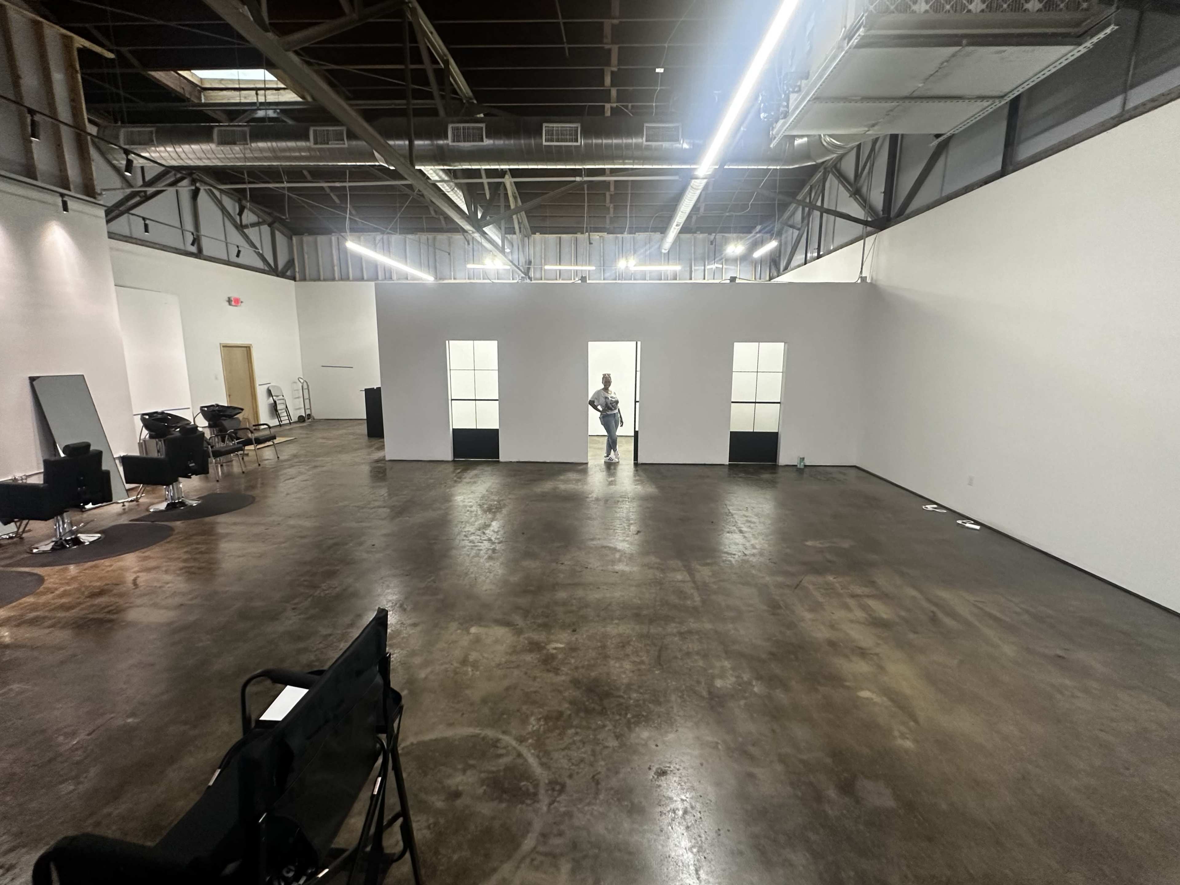 A spacious, empty interior room with polished concrete flooring and white walls, featuring a person standing in the center near mirrored openings.