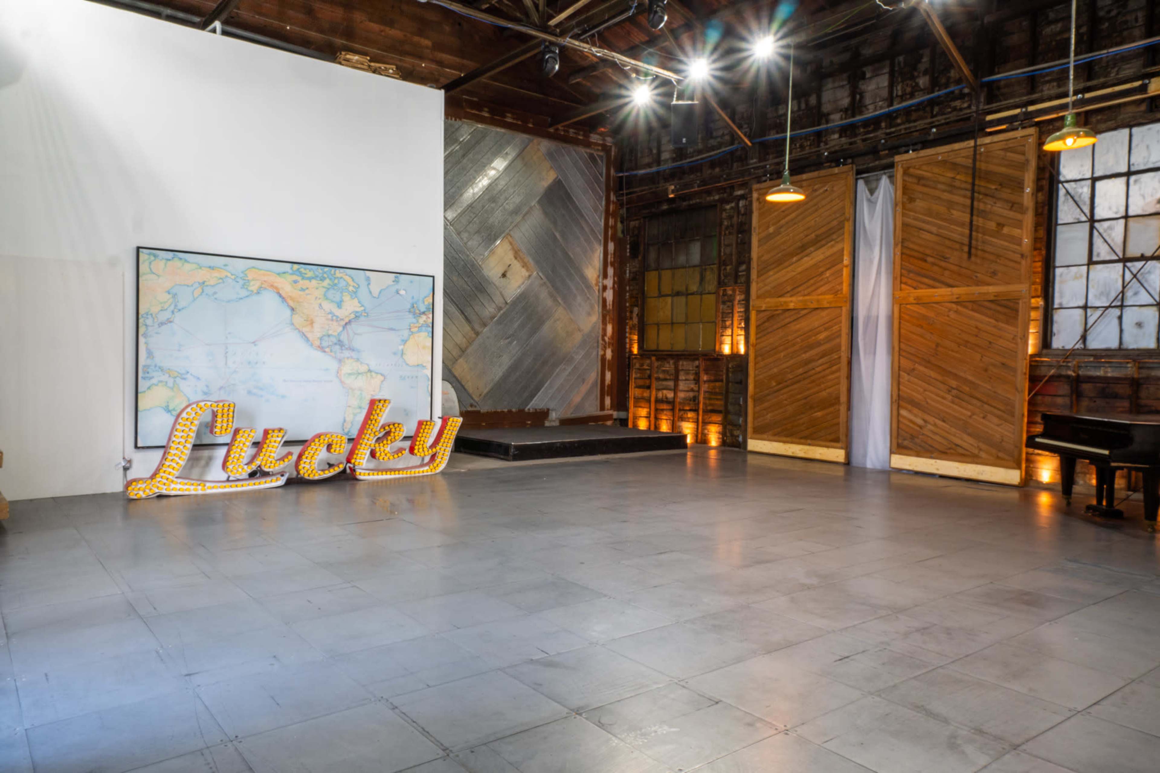 The image shows an empty event space featuring a large world map on the wall, a decorative "Lucky" sign with lights, and wooden paneling in the background.