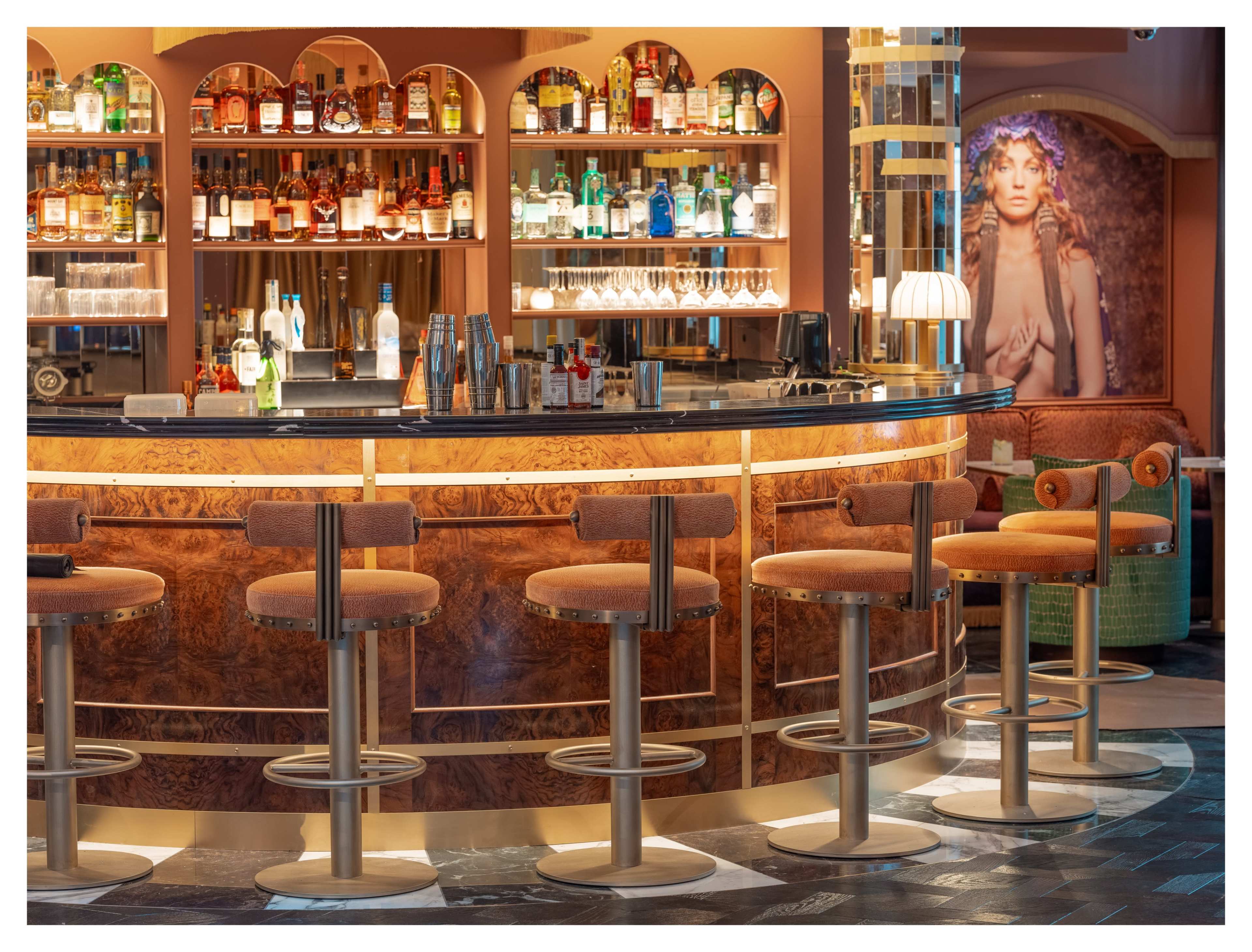 A modern bar features a curved counter with several stools, lined with shelves displaying various bottles of liquor in a stylish setting.