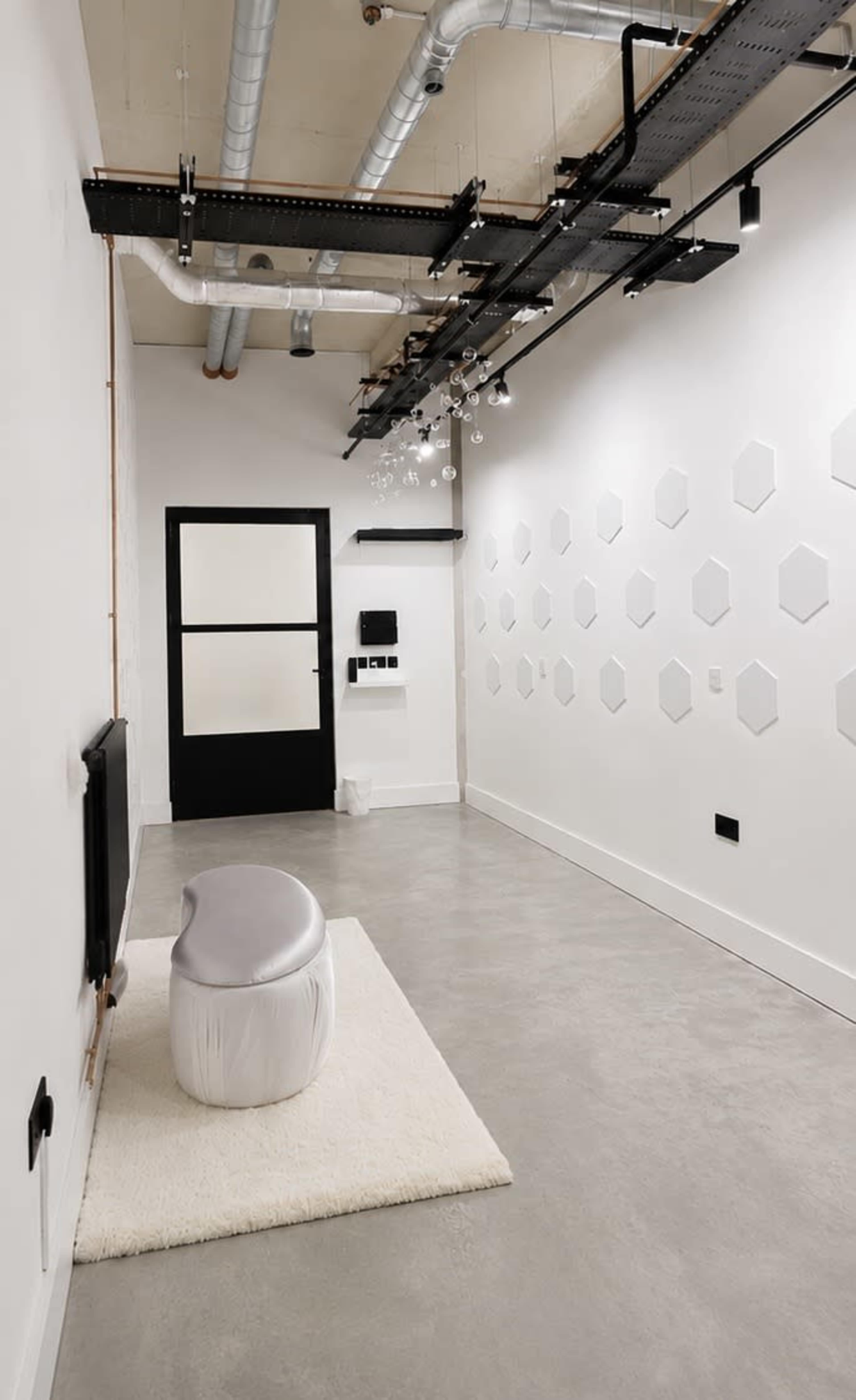 The image shows a modern, minimalist room with a light-colored floor, a white rug, a curved bench, and hexagon-shaped wall decorations.