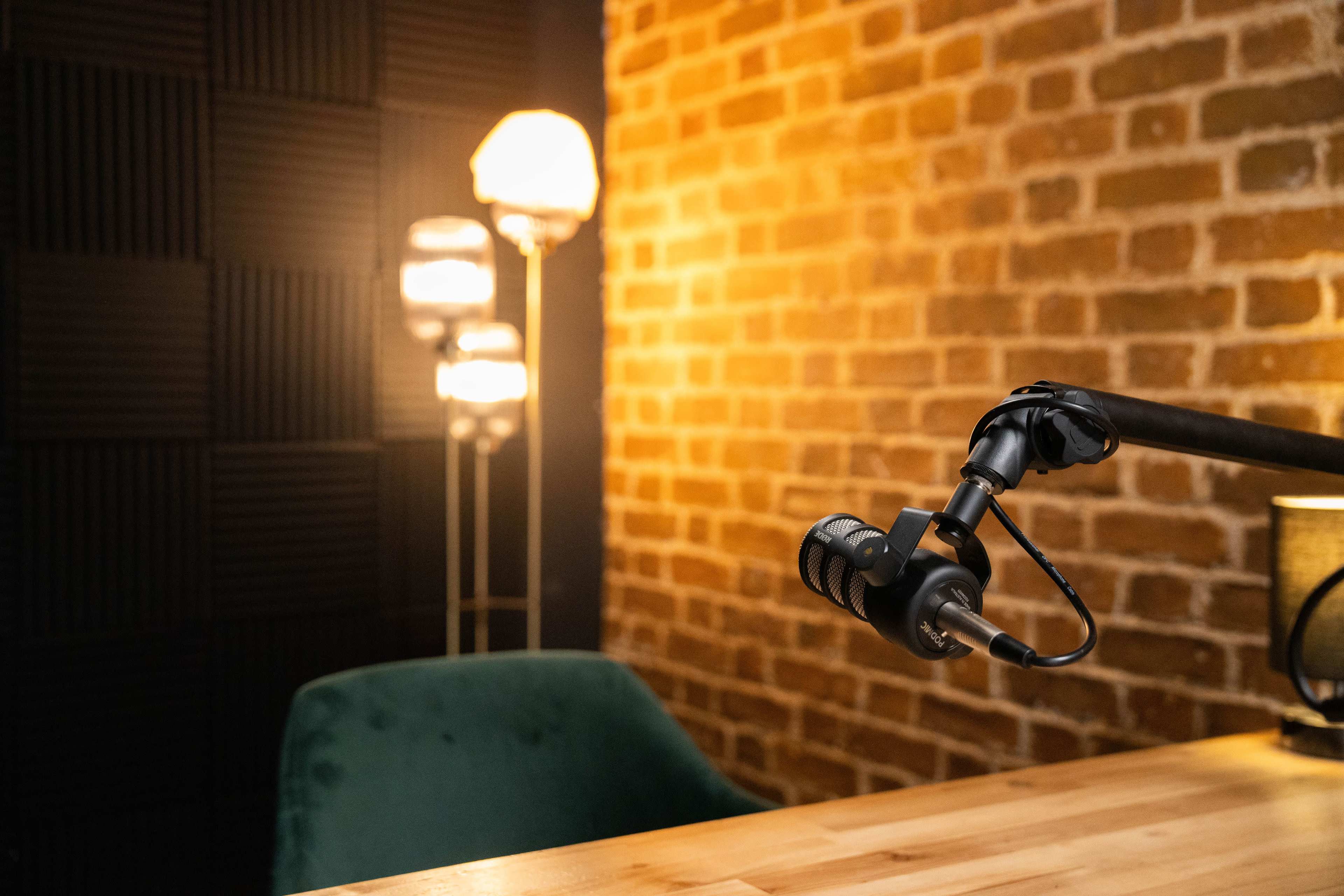 A microphone mounted on a stand in a room with brick walls and soft lighting, accompanied by a green chair and a table.