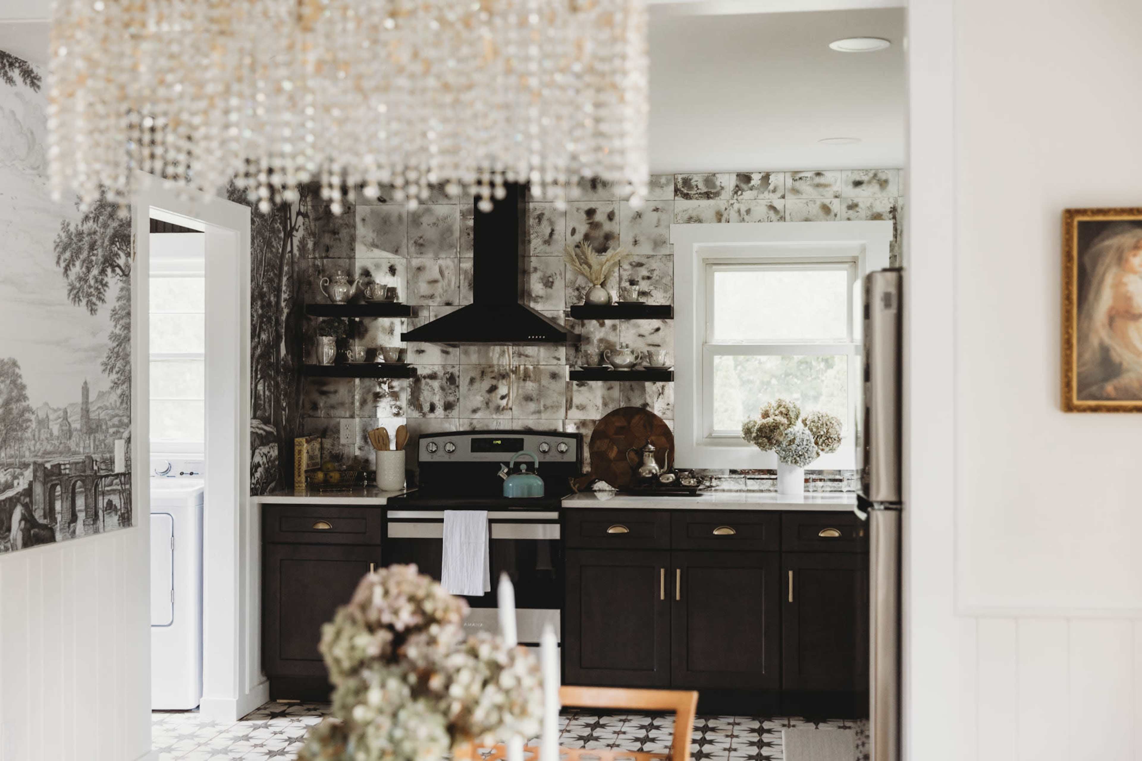 A modern kitchen features dark cabinetry, a stainless steel stove, and a decorative chandelier above a dining table with floral arrangements.