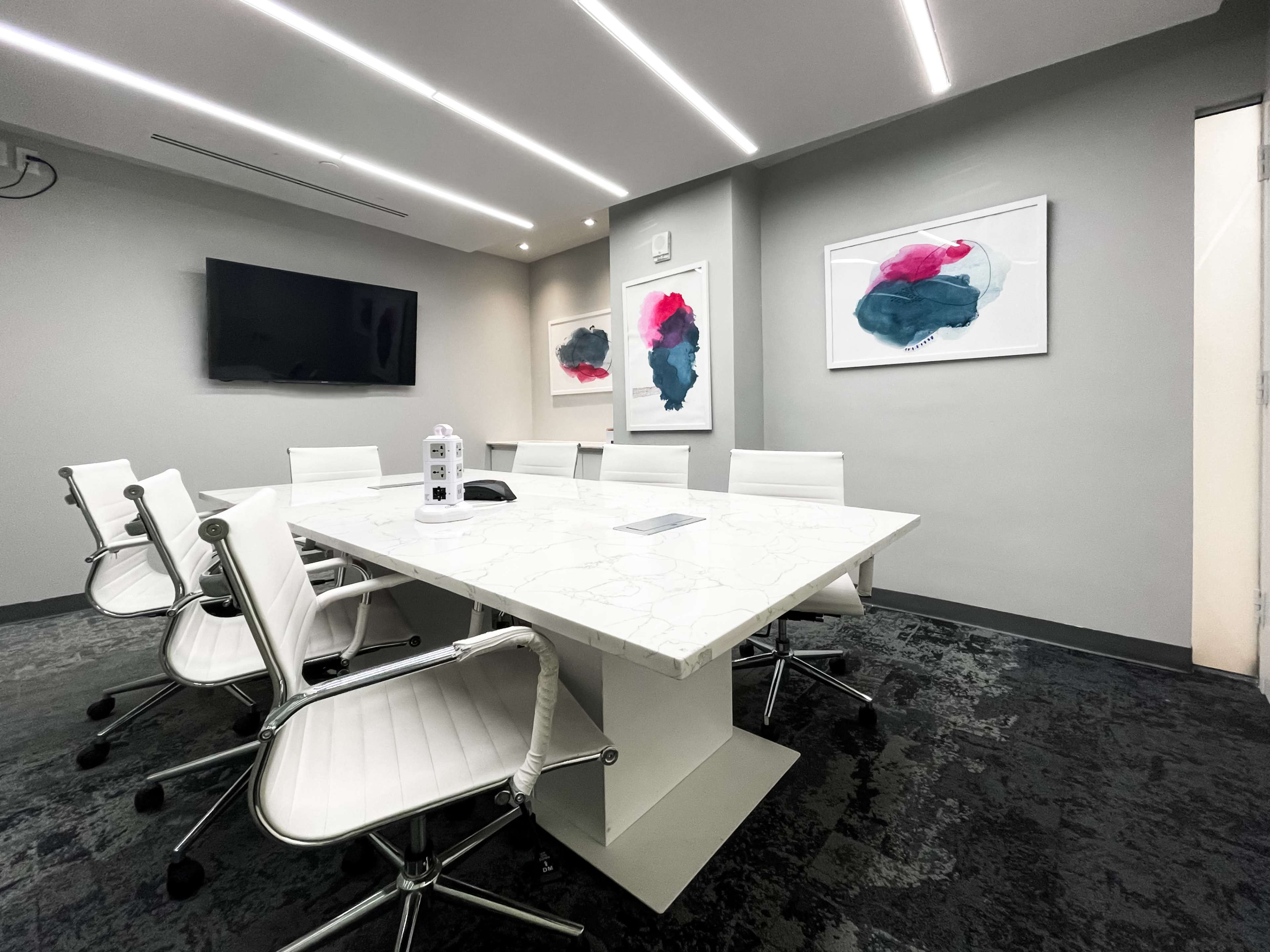 A modern conference room features a white marble table, six white chairs, and two abstract artworks on the walls.