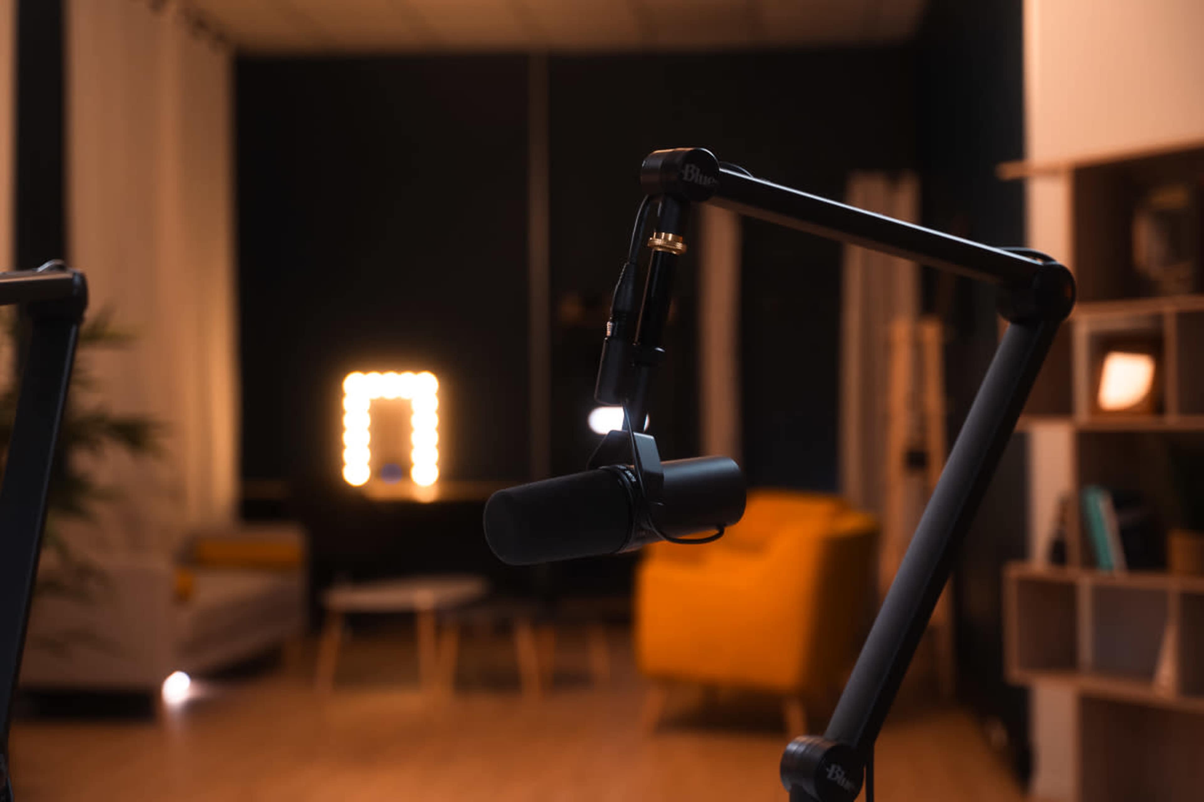 A microphone is positioned on a stand in a dimly lit room with a yellow chair and a vanity mirror in the background.