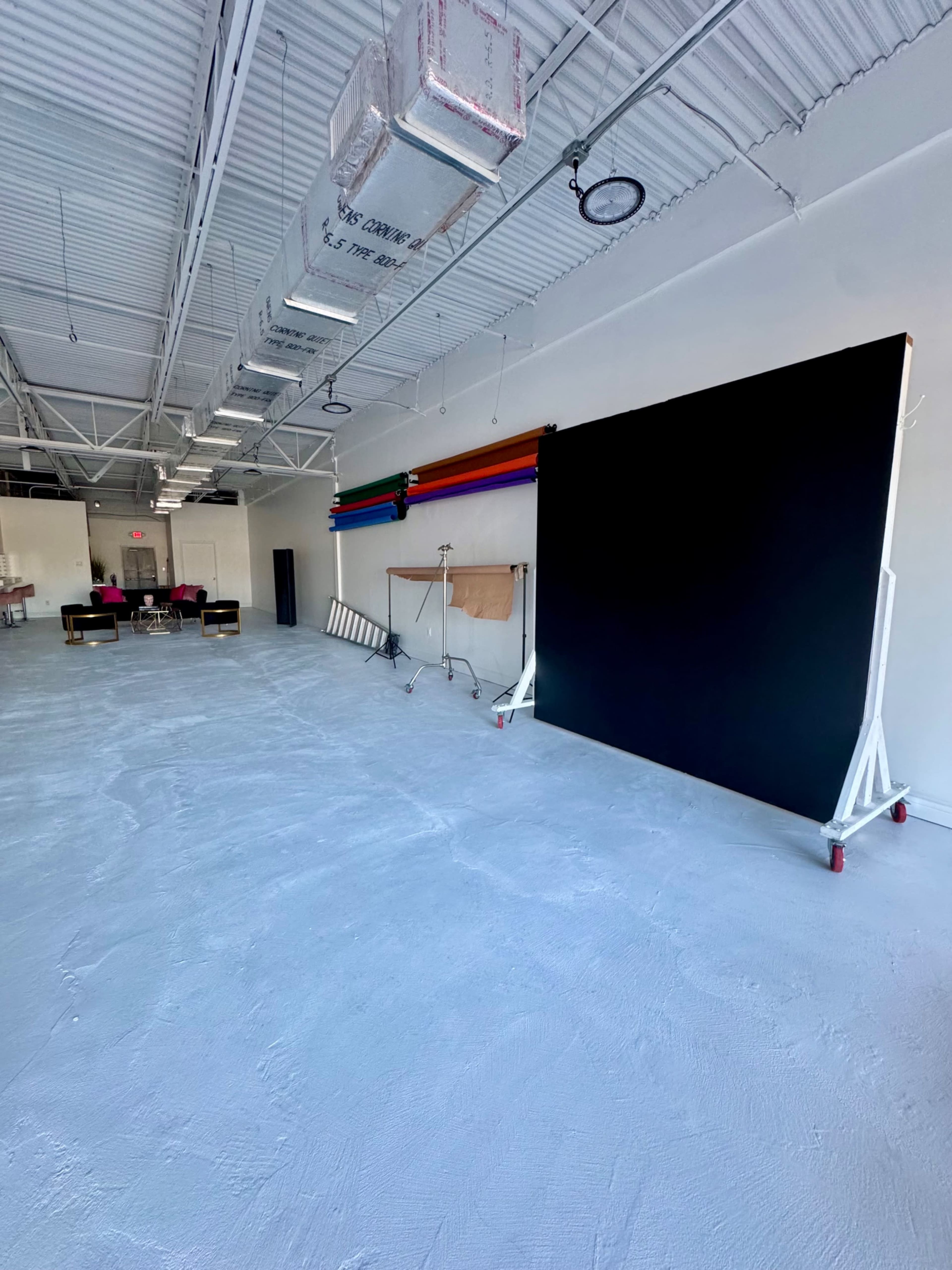 The image depicts a spacious, empty studio with a large black backdrop on a mobile stand and colorful rolls of paper along the wall.