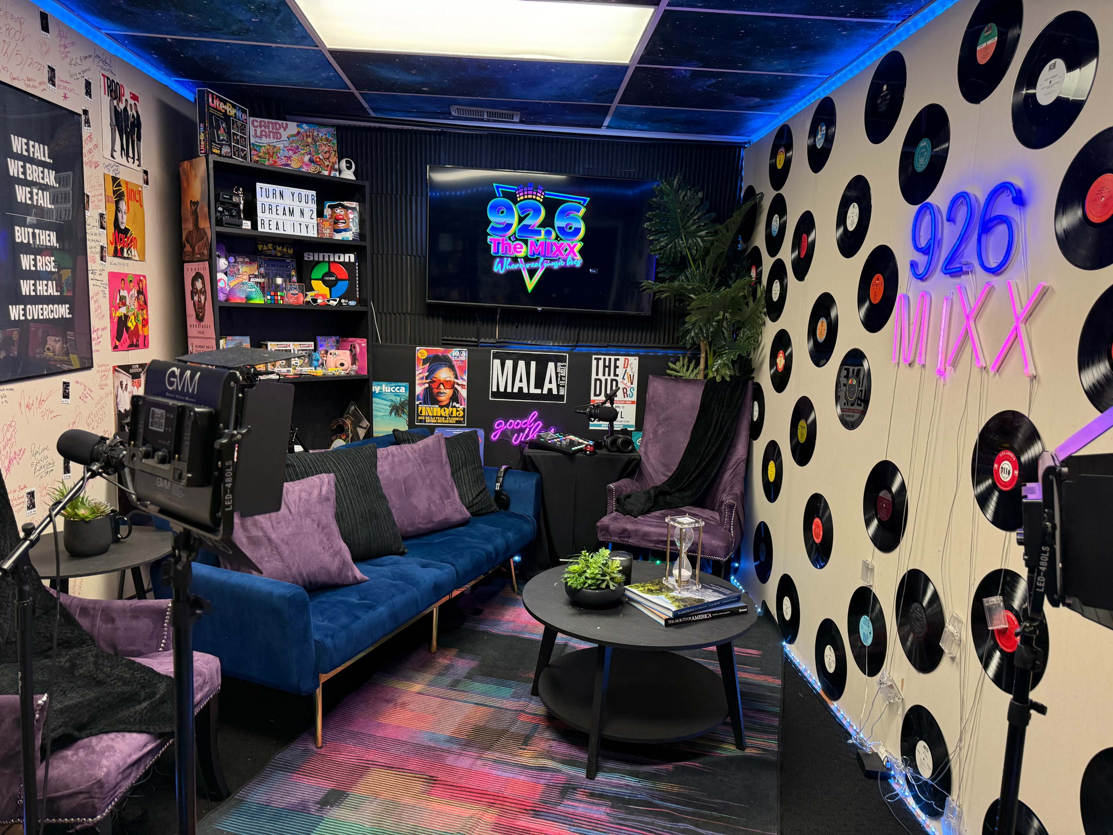 The image shows a stylish media room featuring a blue sofa, black chairs, a television on the wall, and decorations made up of vinyl records.