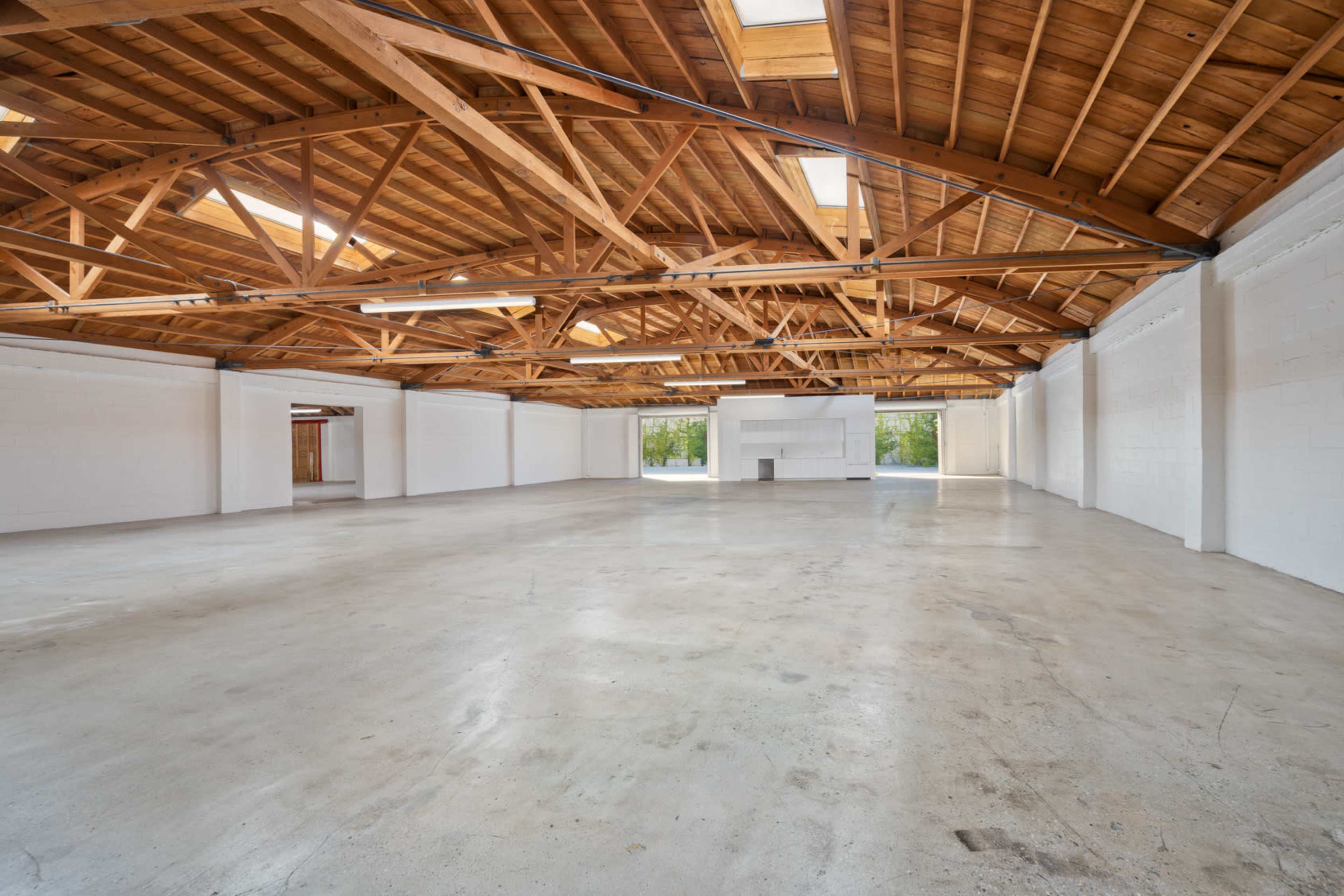 The image shows a spacious, empty warehouse with wooden beams and polished concrete flooring.