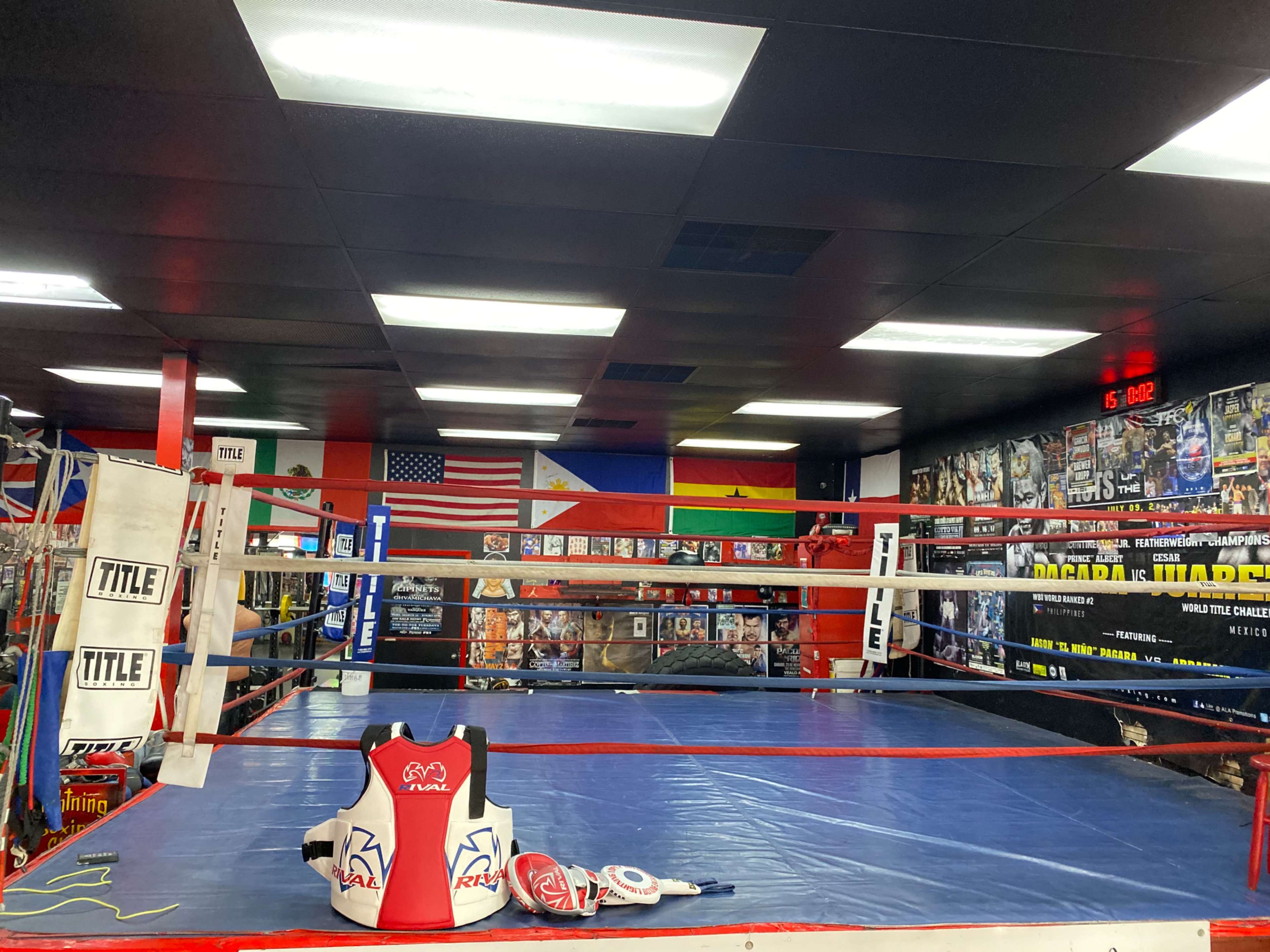 A boxing ring in a gym, surrounded by various flags and posters on the walls.
