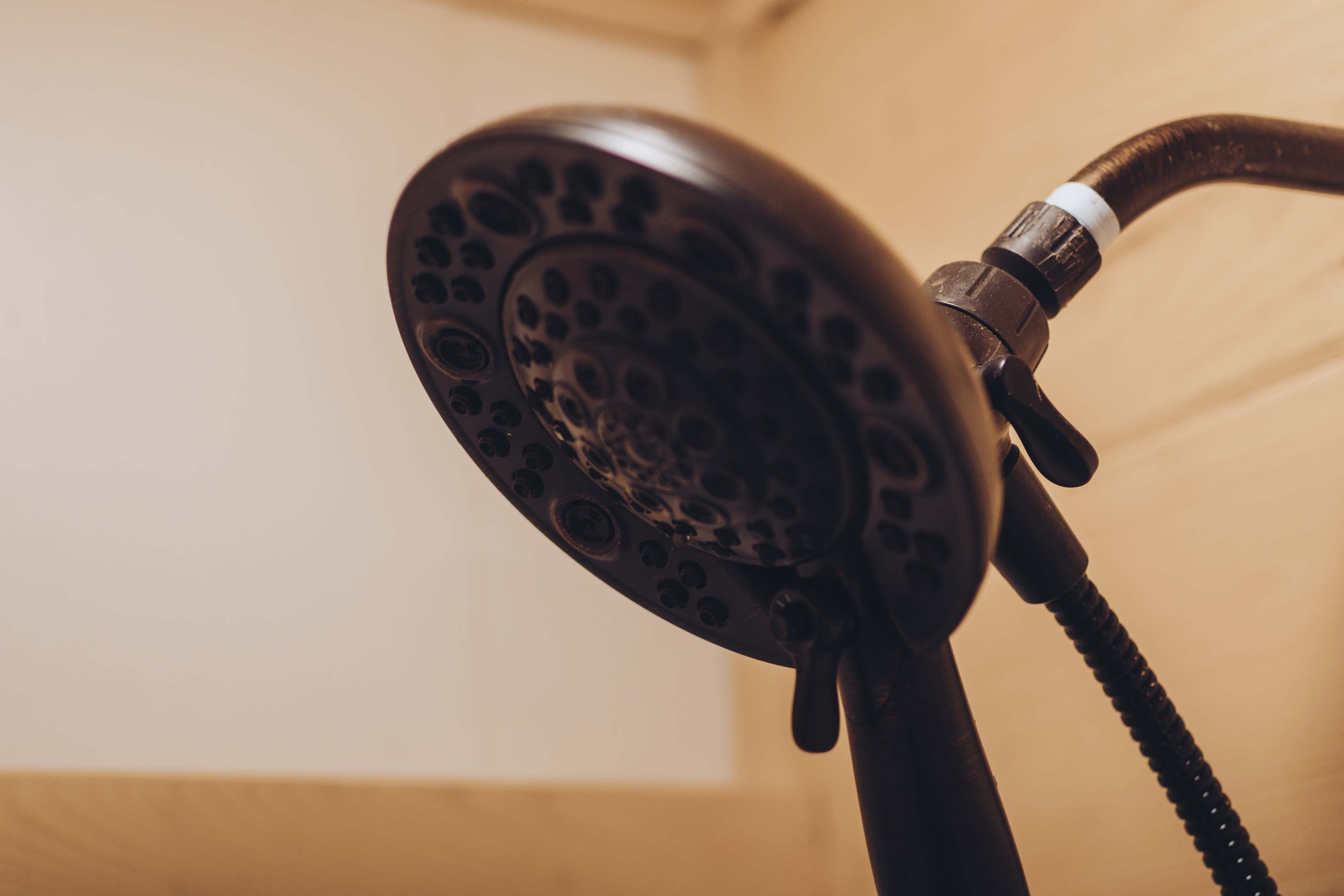 A close-up view of a black showerhead, featuring multiple spray settings, mounted on a pipe in a wooden bathroom setting.