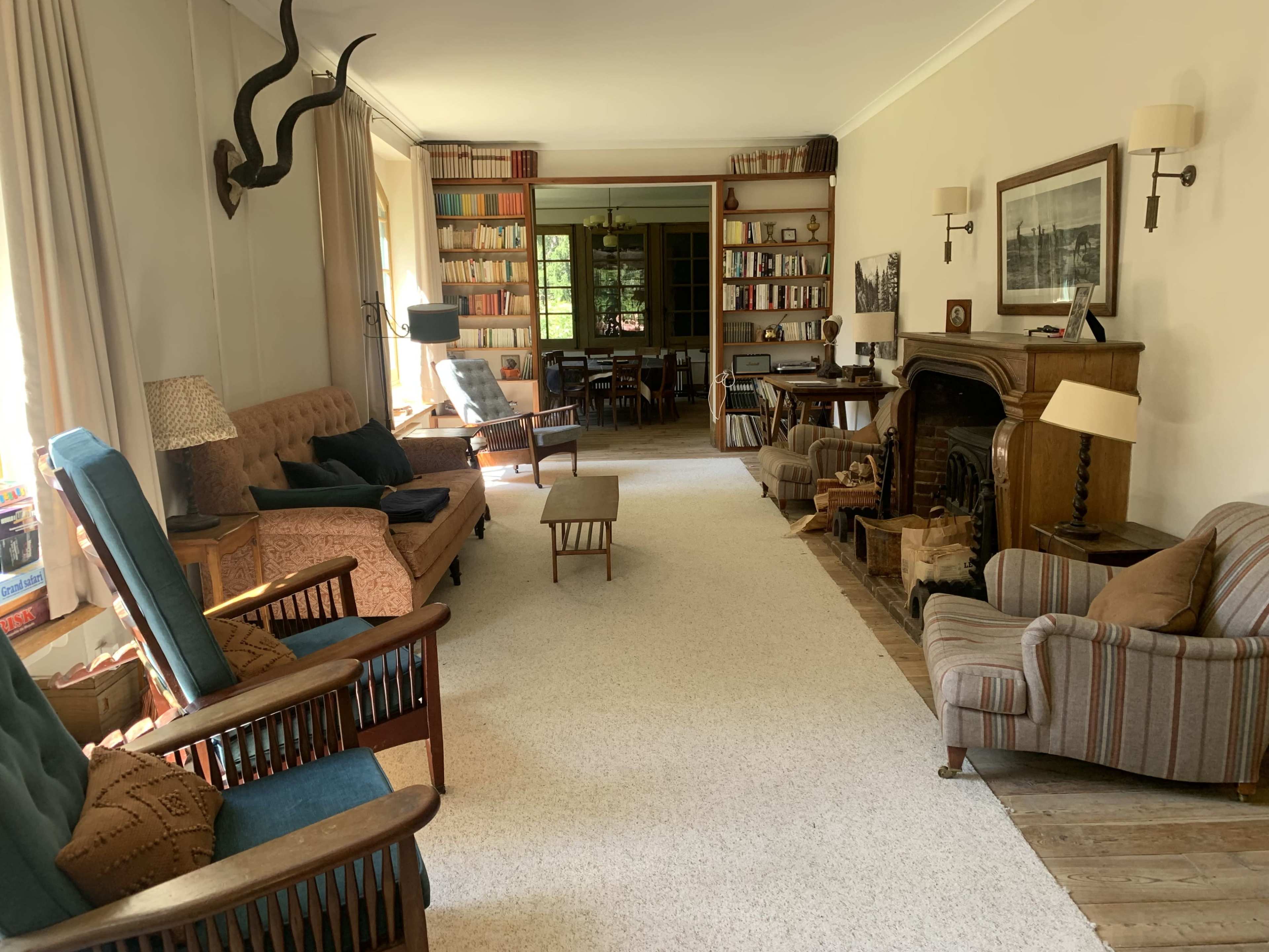 The image shows a spacious living room with various seating arrangements, bookshelves lining the walls, and a fireplace.