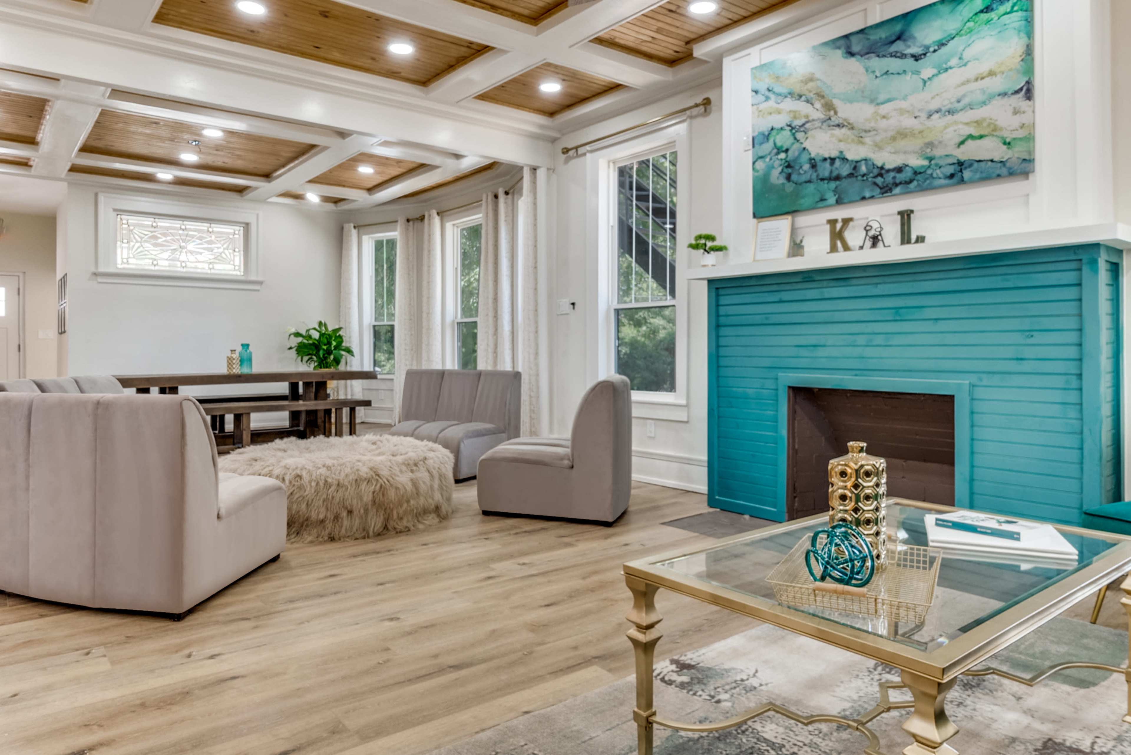 The image shows a spacious living room with a turquoise accent wall, a wood-paneled ceiling, and modern furniture arranged around a central area rug.