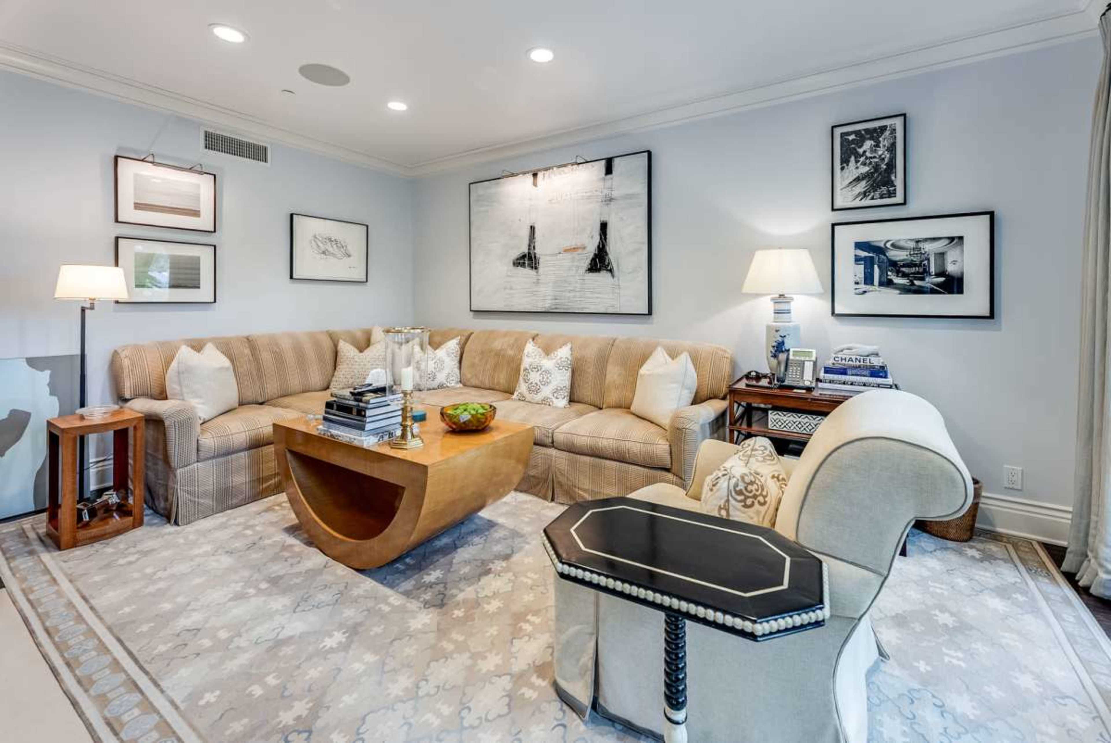 The living room features a curved sectional sofa, a wooden coffee table, and various framed artworks on the walls.