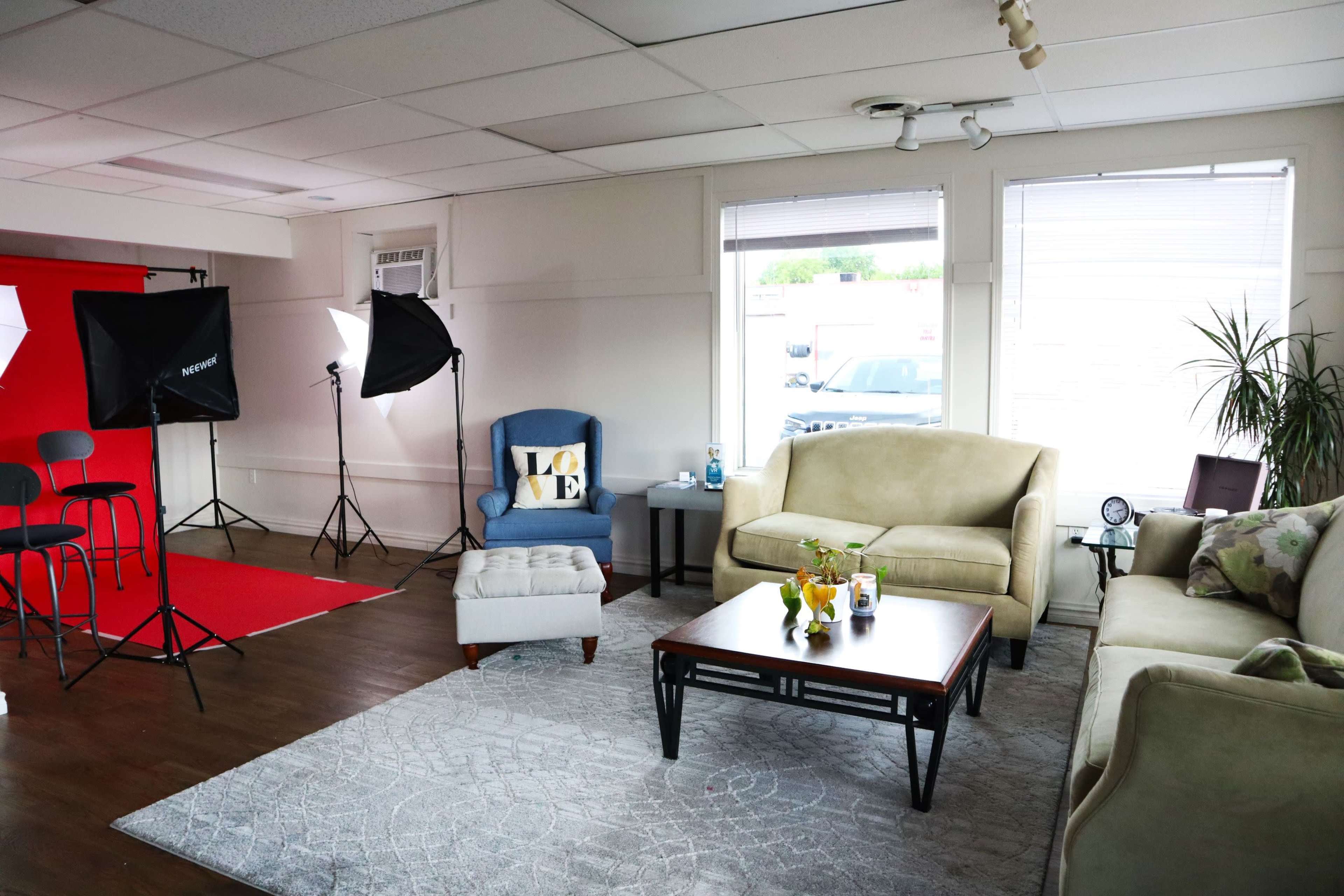 A well-lit studio space with beige sofas, a blue chair, a coffee table, and photography equipment set up in the background.
