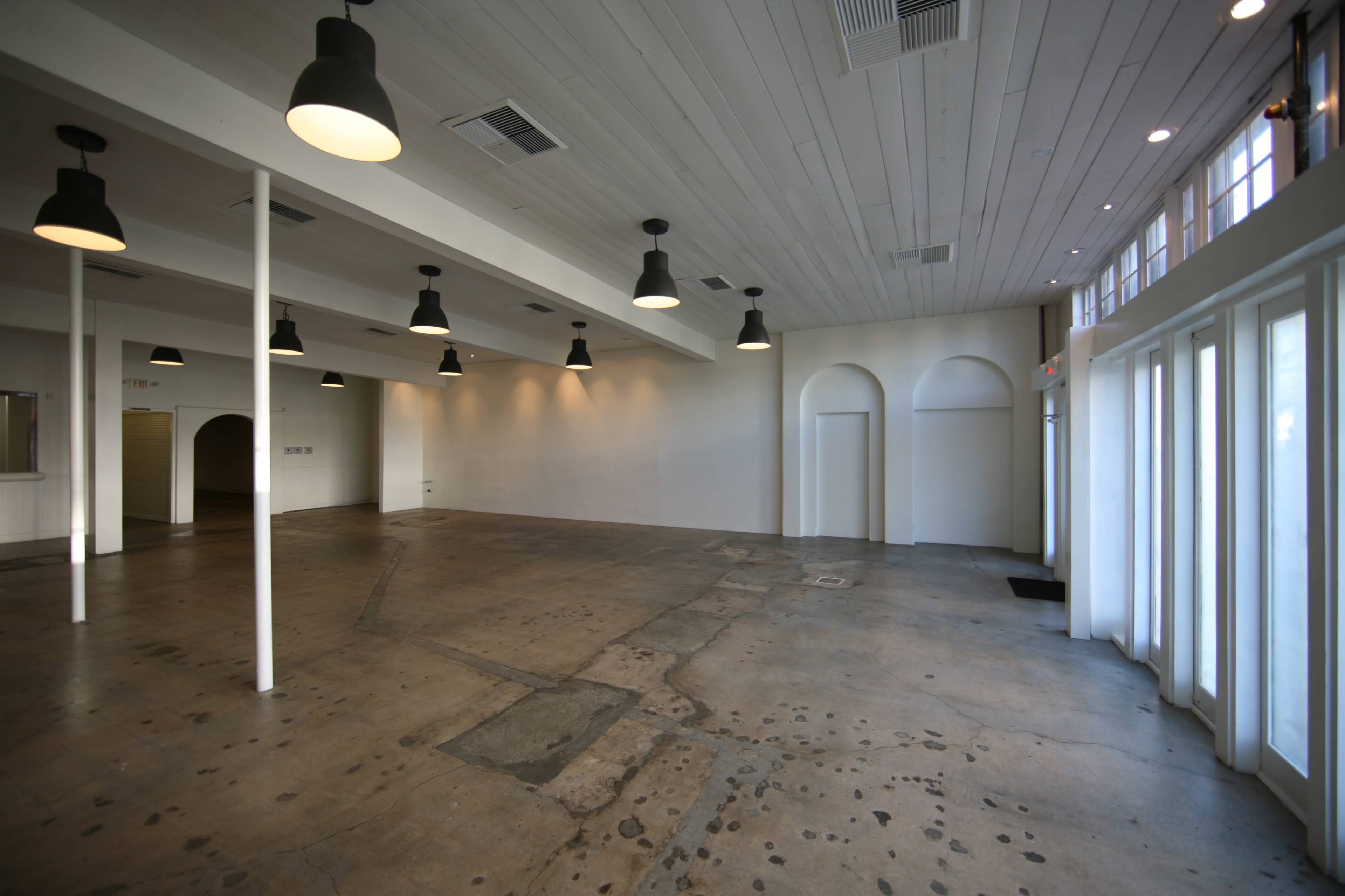 The image shows an empty, spacious room with a concrete floor, white walls, and overhead lighting.